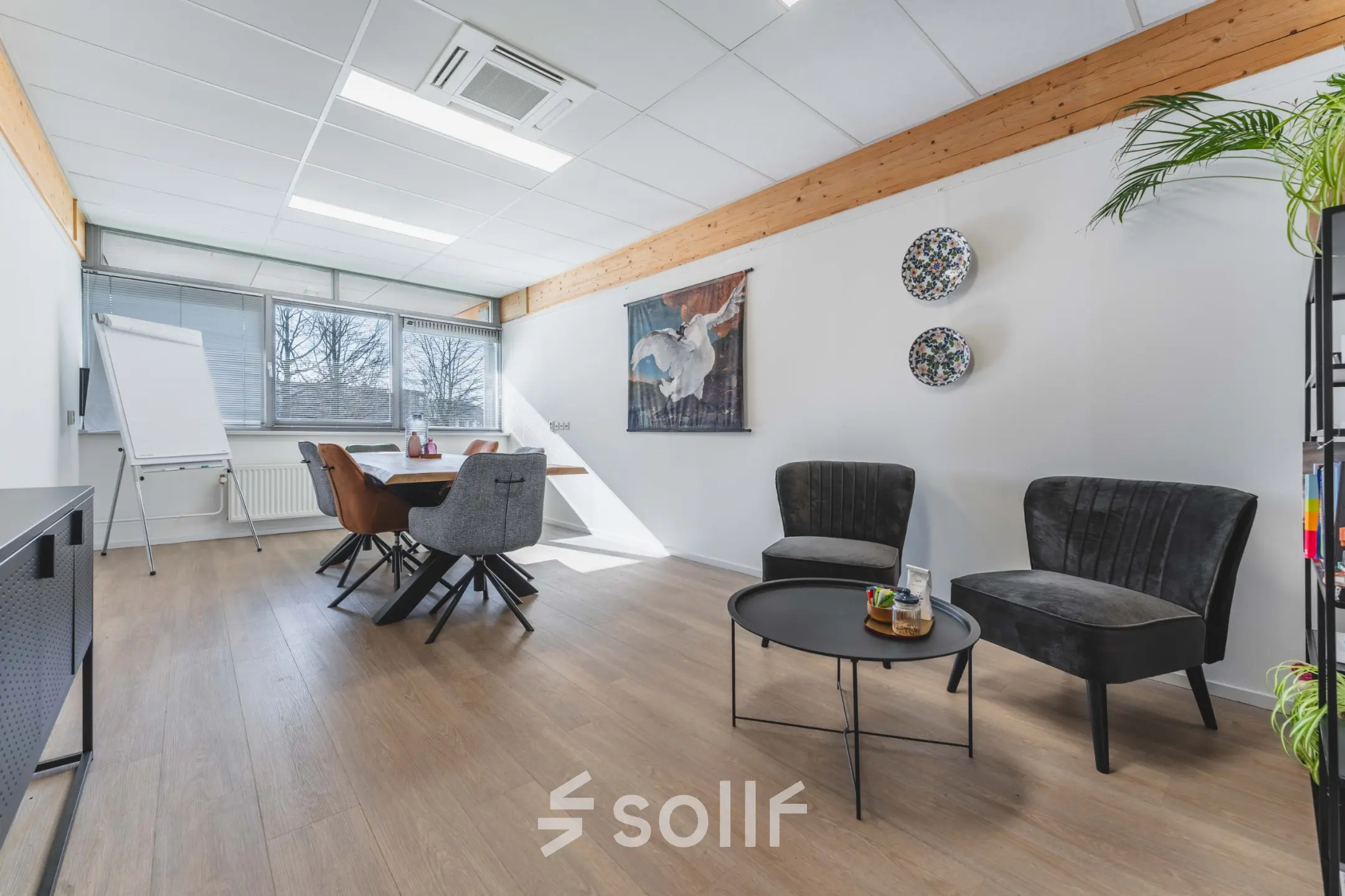 Kantoorruimte te huur aan Steenovenweg 5 in Helmond met een stijlvolle inrichting, waaronder een vergadertafel, stoelen en decoratieve elementen. Grote ramen bieden natuurlijk licht.