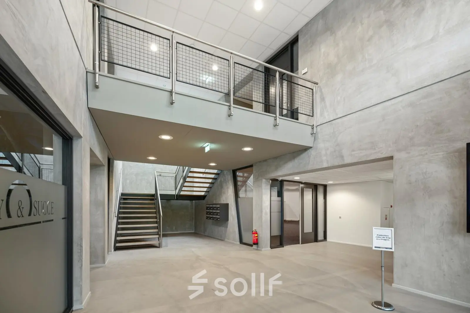 Entree van modern kantoorpand op Lintelerweg 40, Hengelo. Ruime hal met industriële uitstraling en zicht op de trap. Ideaal voor bedrijven die kantoorruimte willen huren.