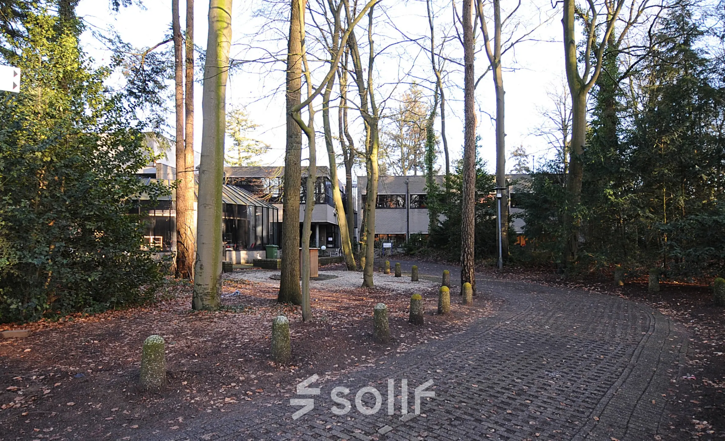 Exterieur van een kantoorpand gelegen aan de Catharina van Renneslaan 8-10 in Hilversum, omringd door bomen en met een geplaveide toegang. Ideaal voor wie een kantoorruimte wil huren in een rustige omgeving.