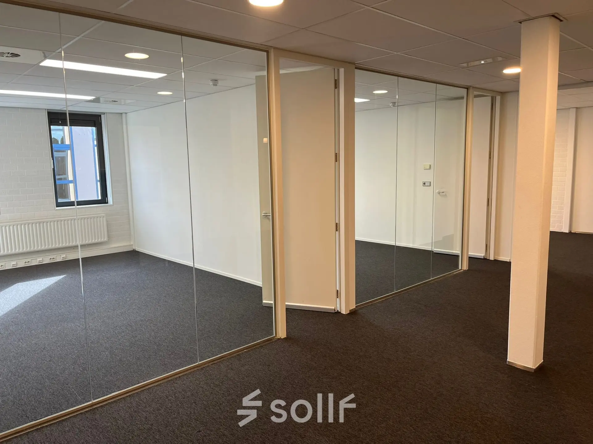Leeg kantoorpand op Catharina van Renneslaan 8-10 in Hilversum, met glazen wanden en grijze vloerbedekking. Ideaal voor bedrijven die kantoorruimte willen huren in een lichte omgeving.