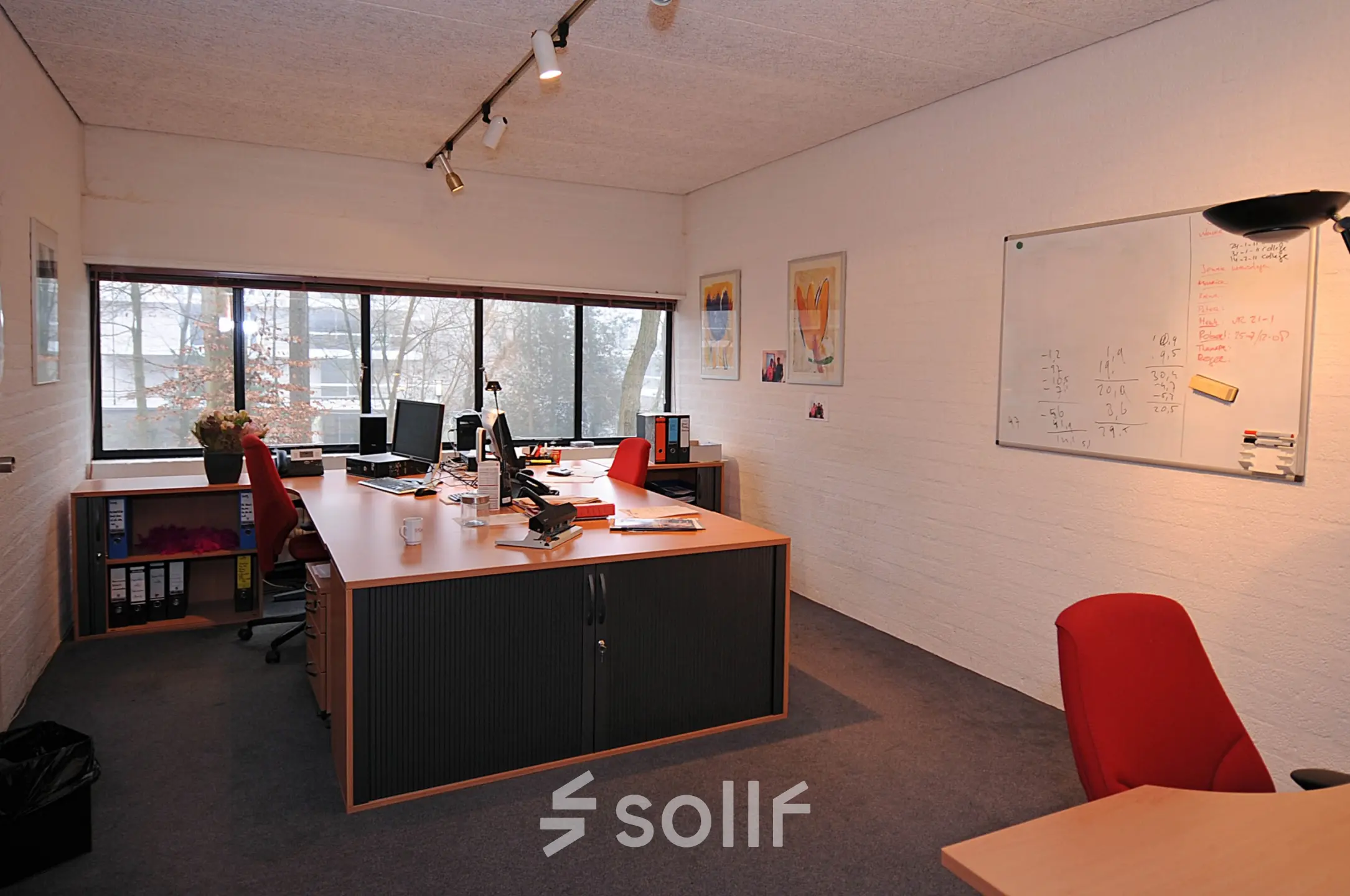 Kantoorruimte te huur aan de Catharina van Renneslaan 8-10 in Hilversum met grote ramen, diverse bureaus en rode stoelen, witte muren en een whiteboard.