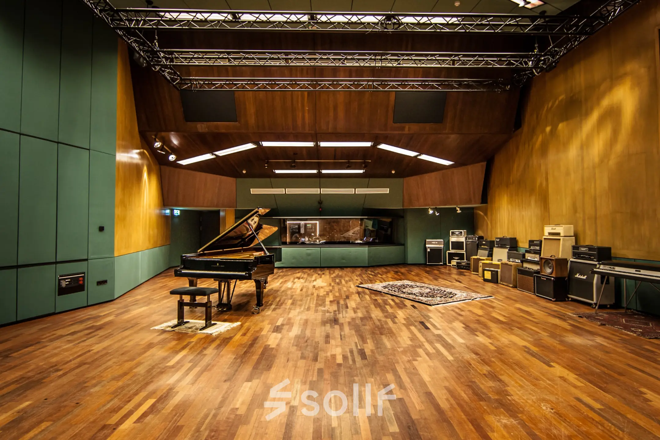 Ruime opnamestudio met een vleugelpiano op een houten vloer, omgeven door geluidsapparatuur. Ideale plek voor muziekproductie of creatieve kantoorruimte huren in Hilversum.