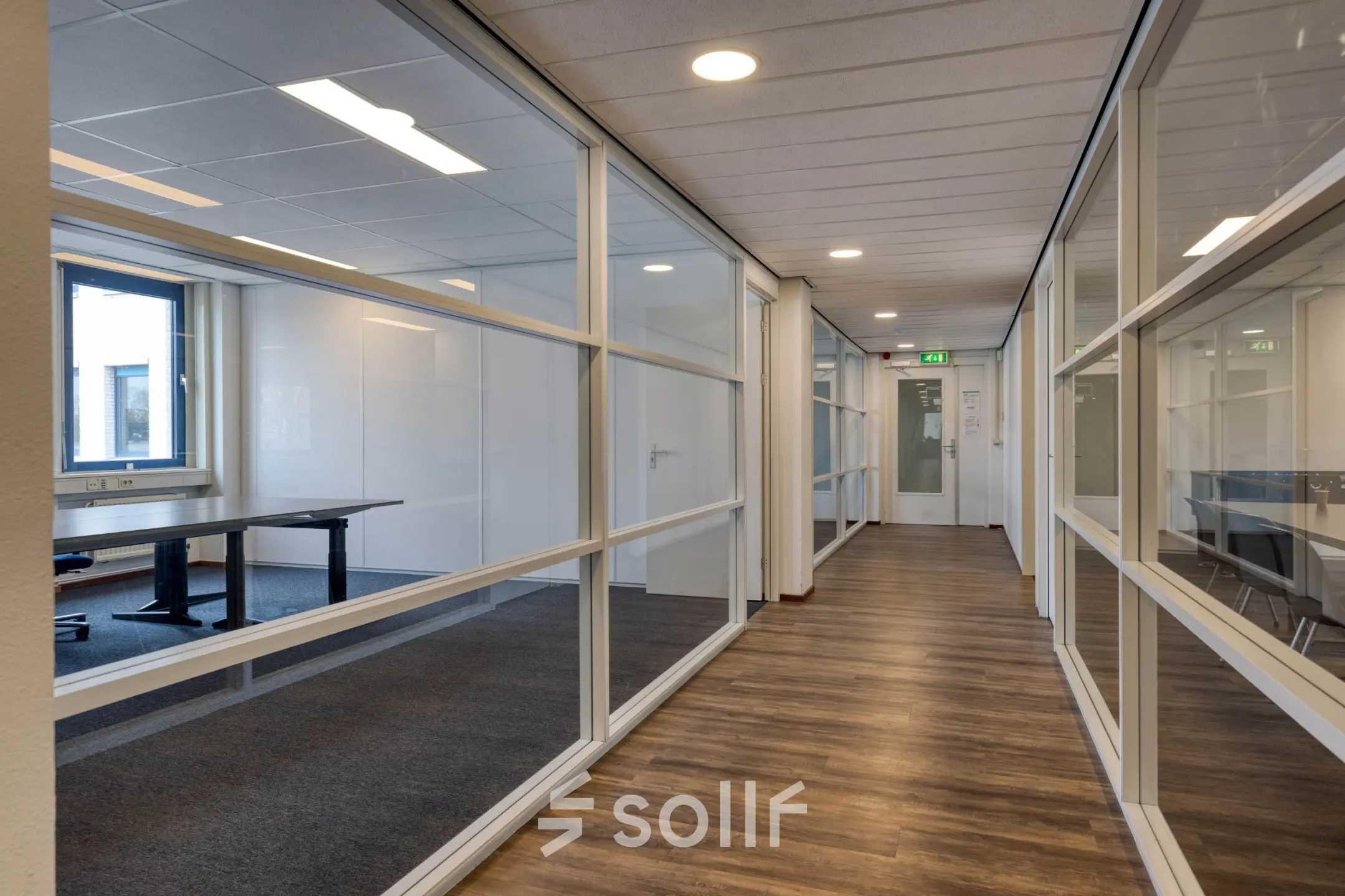 Glazen wanden verdelen de kantoorruimte op Franciscusweg 219 in Hilversum met houten vloeren en zicht op ramen langs de gang.