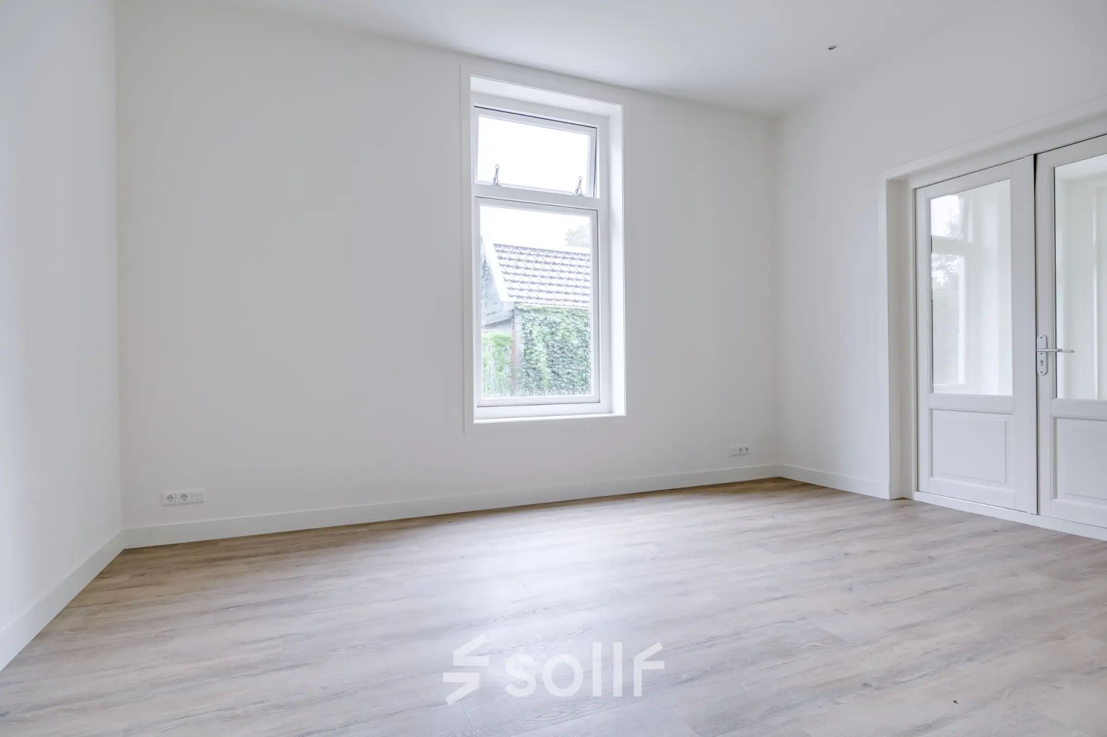 Lichte kantooruimte te huur op Graaf Florislaan 40, Hilversum. De ruimte is ongemeubileerd en heeft een groot raam, houten vloeren en dubbele deuren, ideaal voor kantoorinrichting.