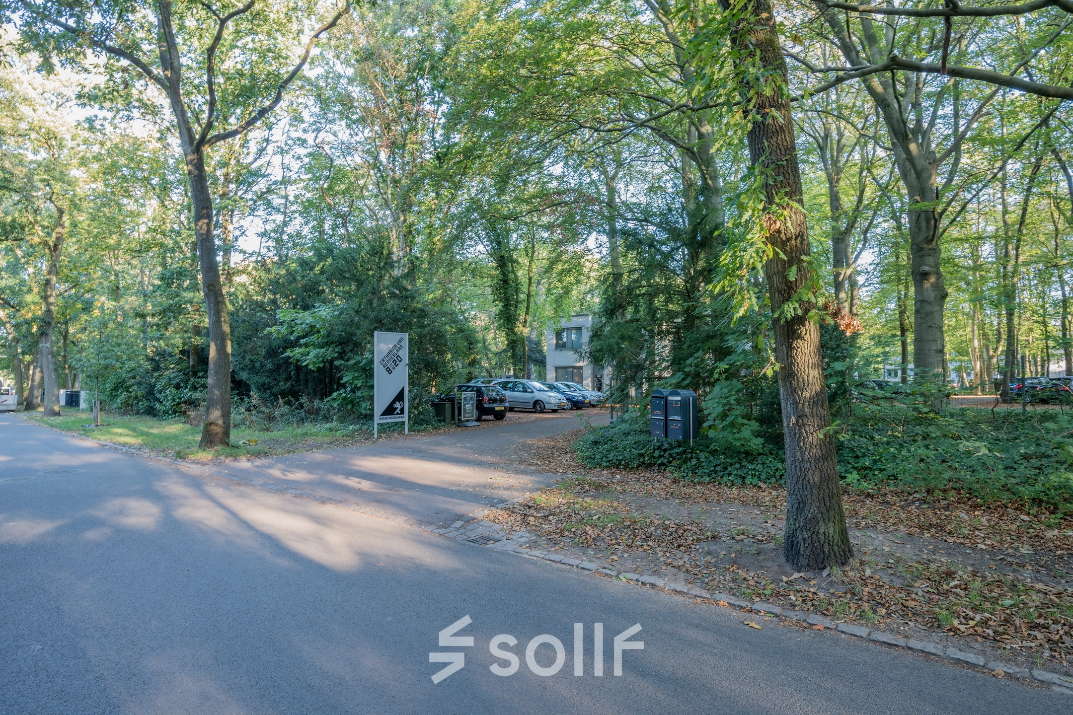 Buitenzicht op het kantoorpand gelegen aan de groene Mozartlaan 25 in Hilversum, omgeven door bomen en met een parkeerplaats vooraan.