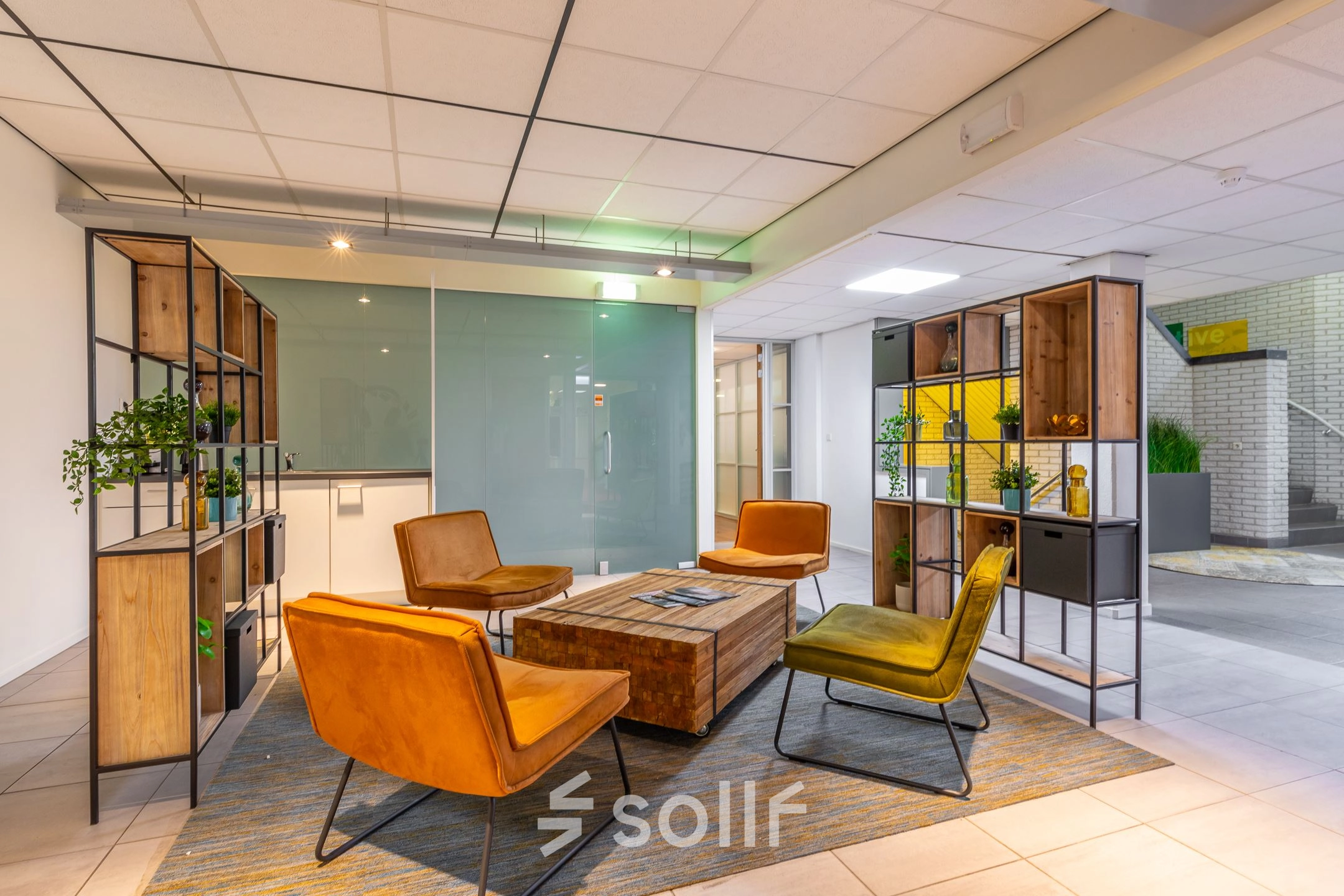 Moderne kantoorlounge in Hilversum met houten rekken, kleurrijke stoelen en een glazen wand, ideaal voor ontspanning tijdens de werkdag. Kantoorruimte huren met verfijnde inrichting.
