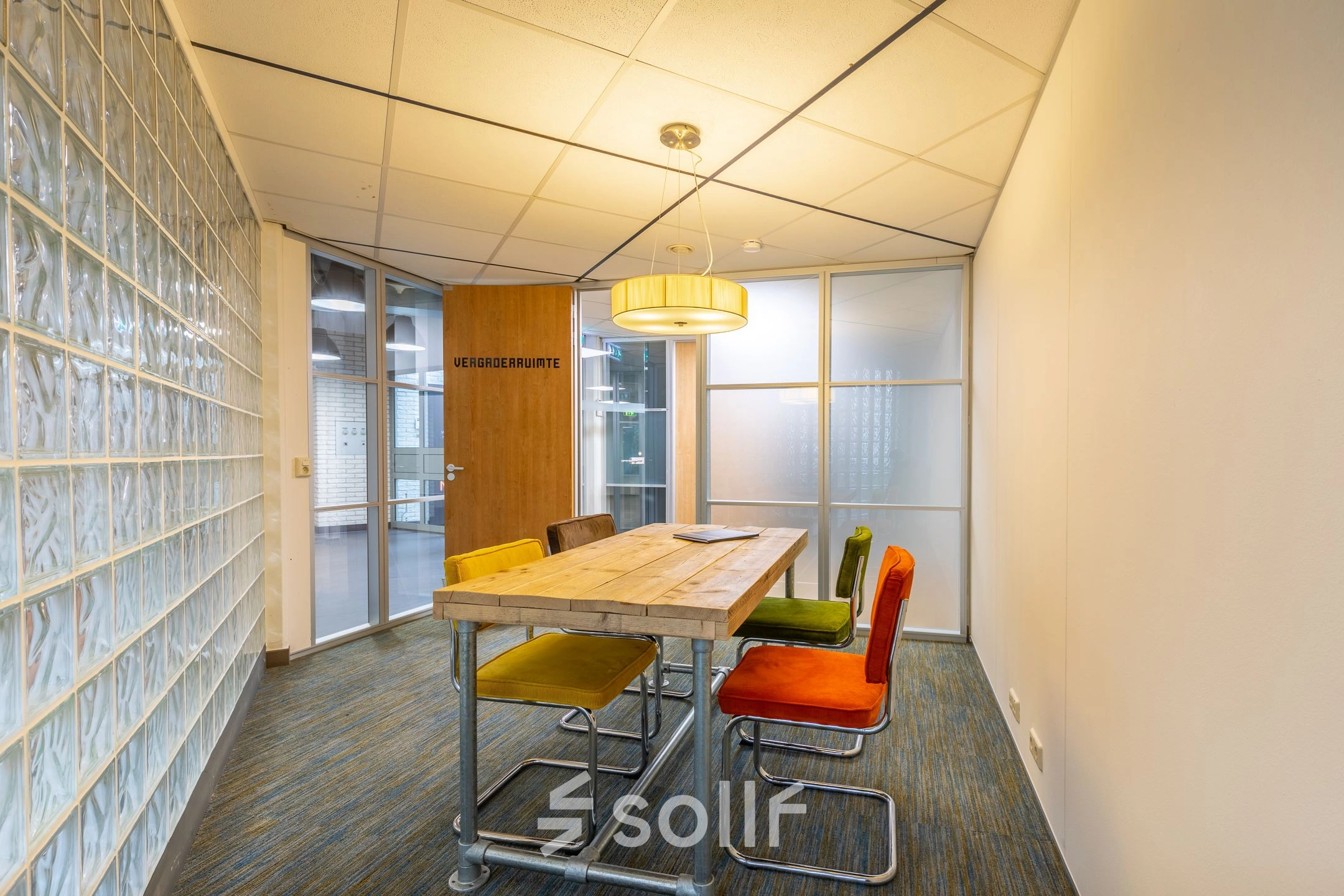 Vergaderruimte in kantoorpand op Mozartlaan 25 in Hilversum met houten tafel en kleurrijke stoelen, ideaal voor wie kantoorruimte wil huren.