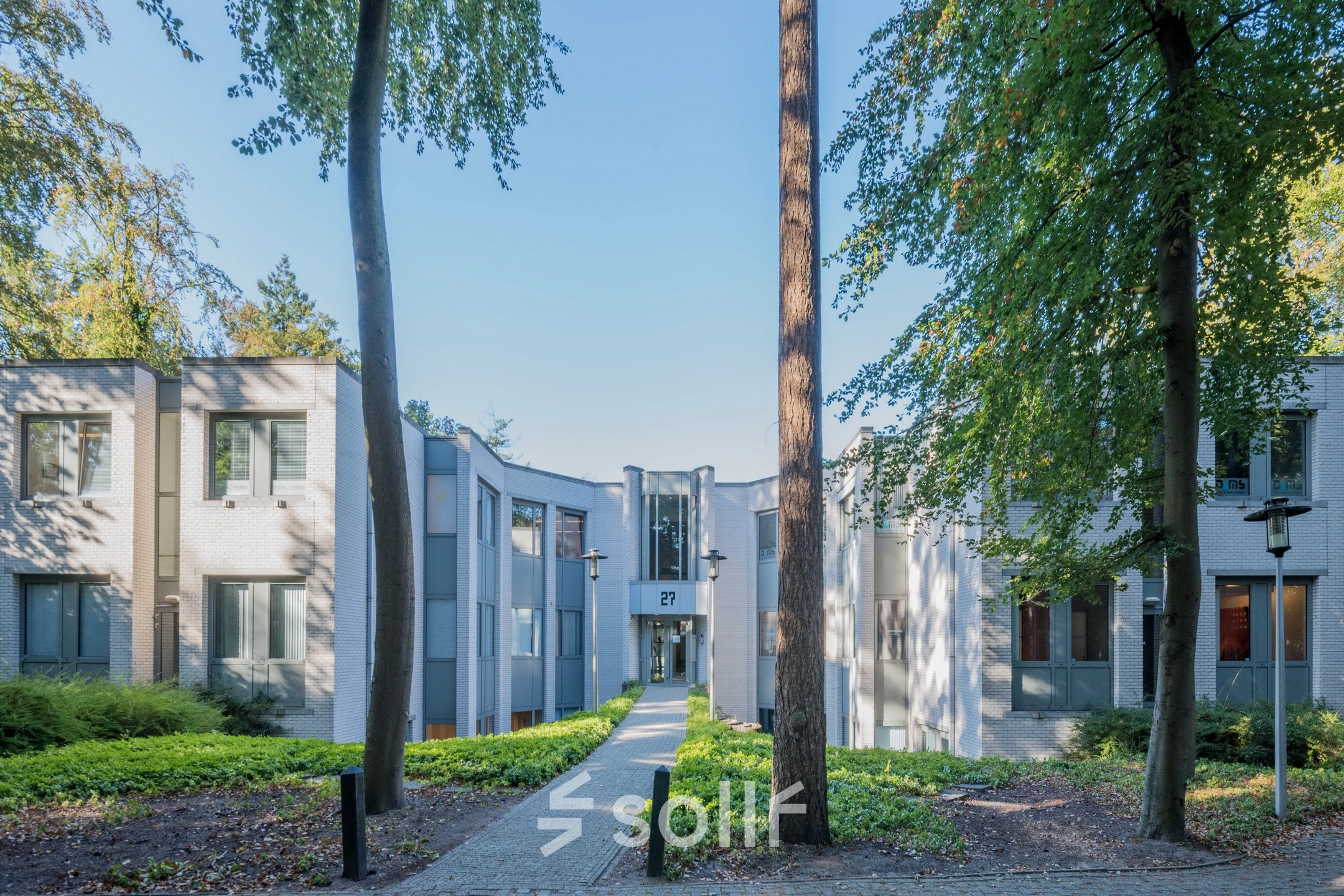 Het kantoorpand aan de Mozartlaan 27 in Hilversum, omgeven door groen en bomen, met een pad naar de entree. Ideale optie voor kantoorruimte huren.