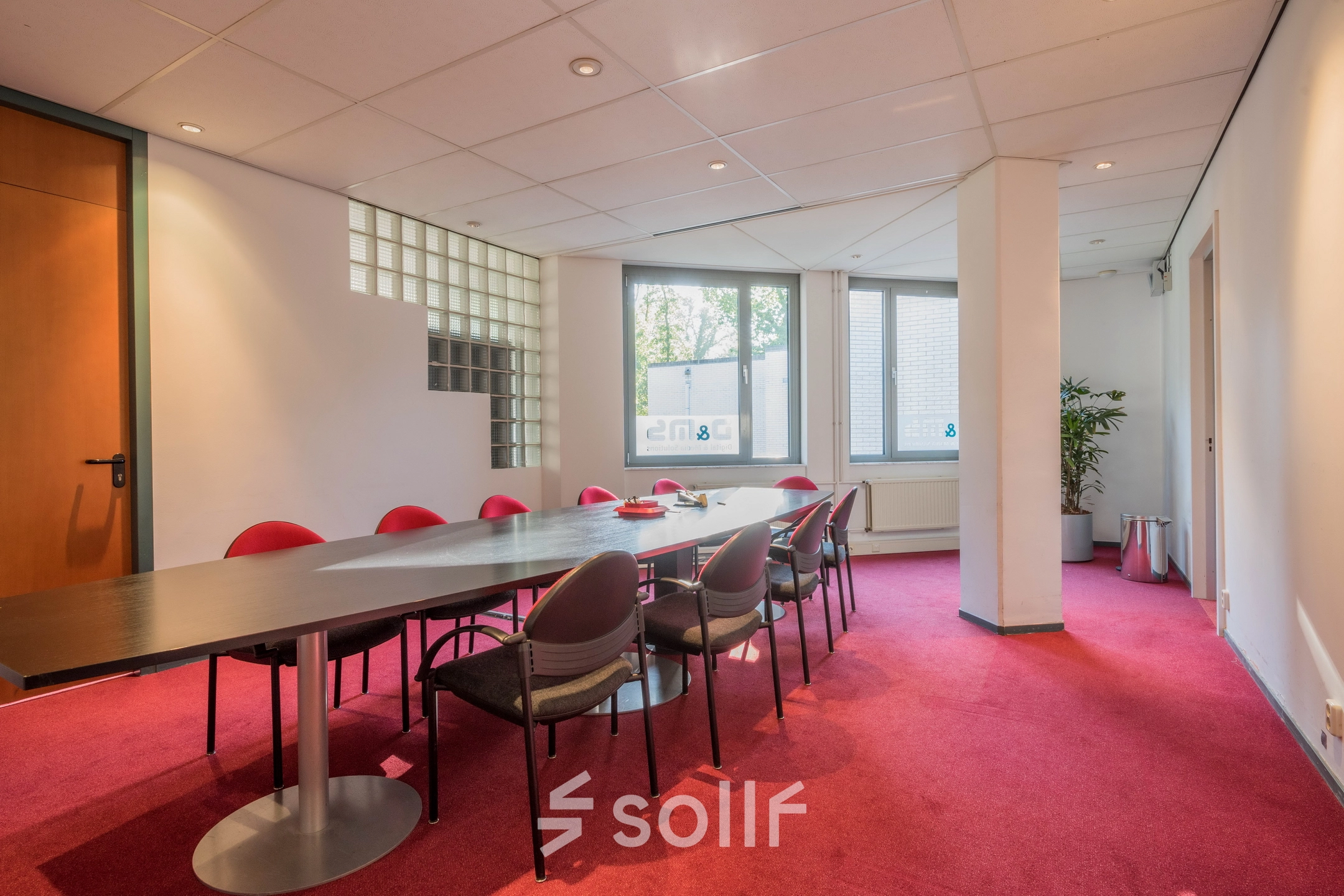 Vergaderruimte in het kantoorpand op Mozartlaan 27, Hilversum met rode vloerbedekking en een lange tafel omringd door stoelen.
