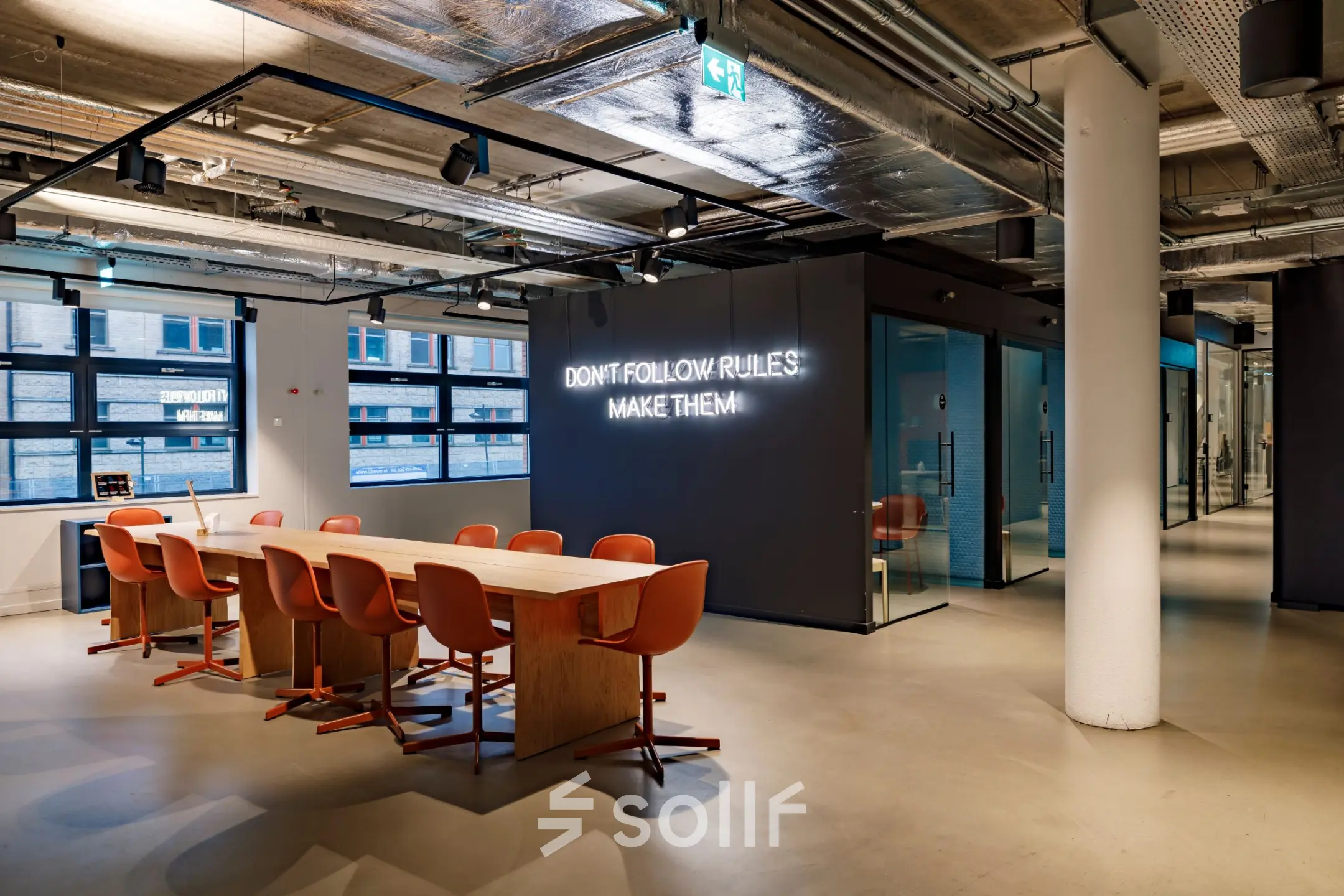 Moderne kantoorruimte op Siriusdreef 16 in Hoofddorp met een lange tafel en oranje stoelen, geschikt voor vergaderingen of teamwerk. De muur heeft inspirerende tekst, ideaal voor wie kantoorruimte wil huren.