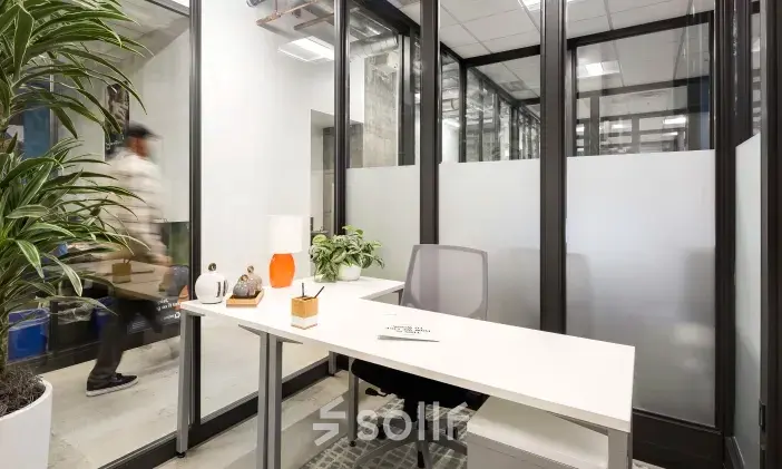 Moderne kantoorruimte te huur op Siriusdreef 17 in Hoofddorp, met een transparante glaswand en minimalistische inrichting. Een persoon loopt voorbij de kantoorruimte, ideaal voor zakelijke activiteiten.