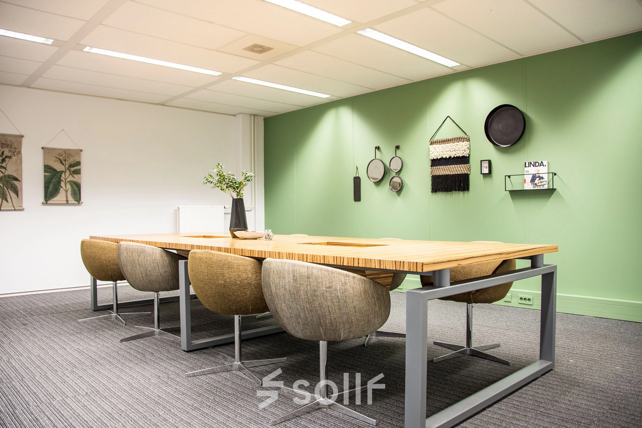 Moderne vergaderruimte in kantoorpand op Meidoornkade 22, Houten met lange houten tafel en comfortabele stoelen, tegen een groene wand met decoraties. Ideaal voor kantoorruimte huren.