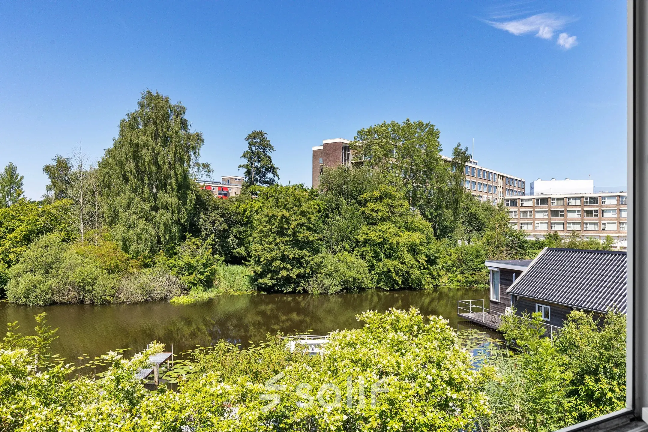 Uitzicht op de groene omgeving van kantoorpand aan de Ouddeelstraat 7a, Leeuwarden, met water en omringende gebouwen.