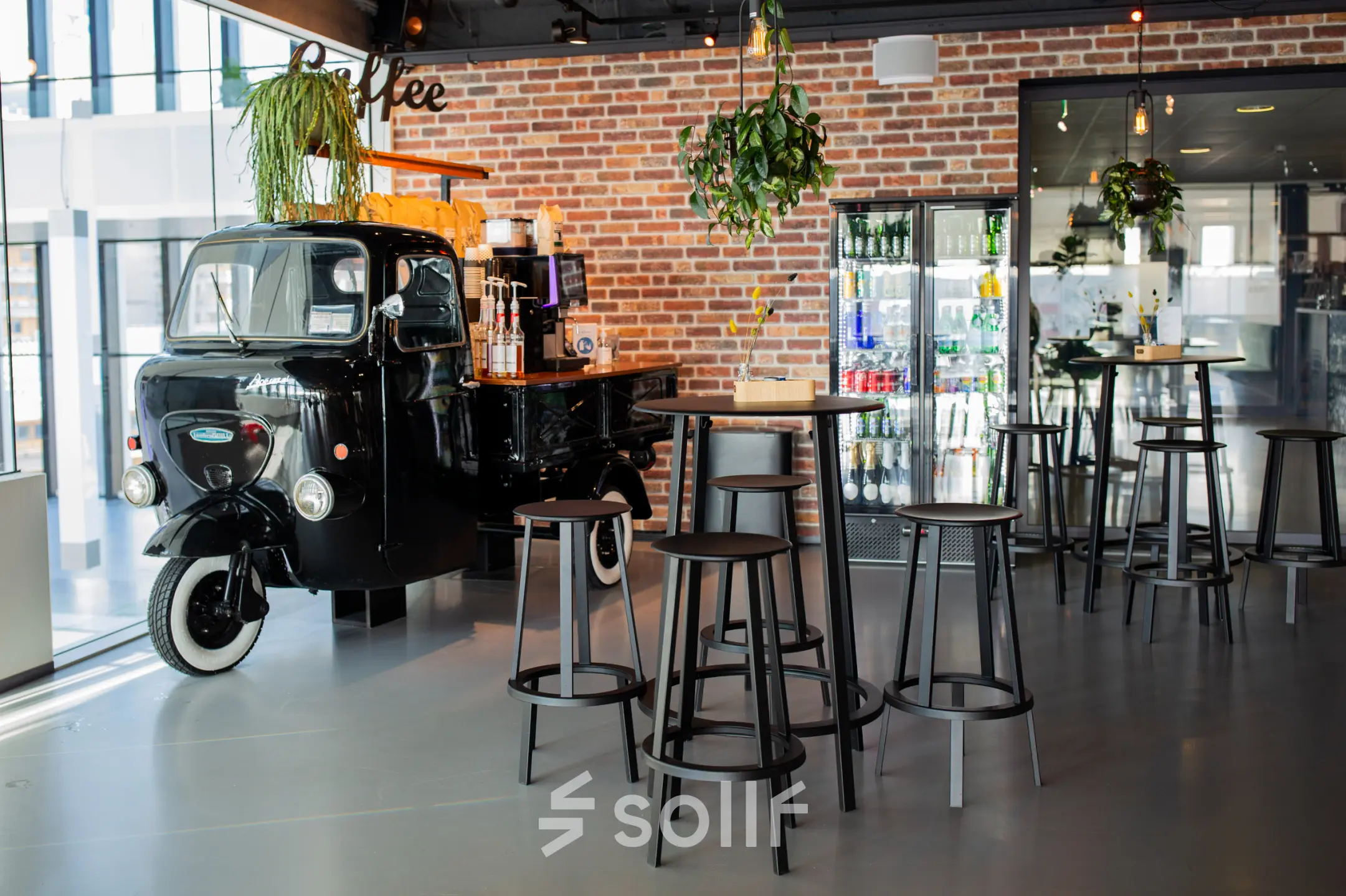 Unieke kantoorruimte te huur in Leiden, Bargelaan 200, met een stijlvolle bar en vintage koffieauto, omringd door hoge krukken en hangende planten.