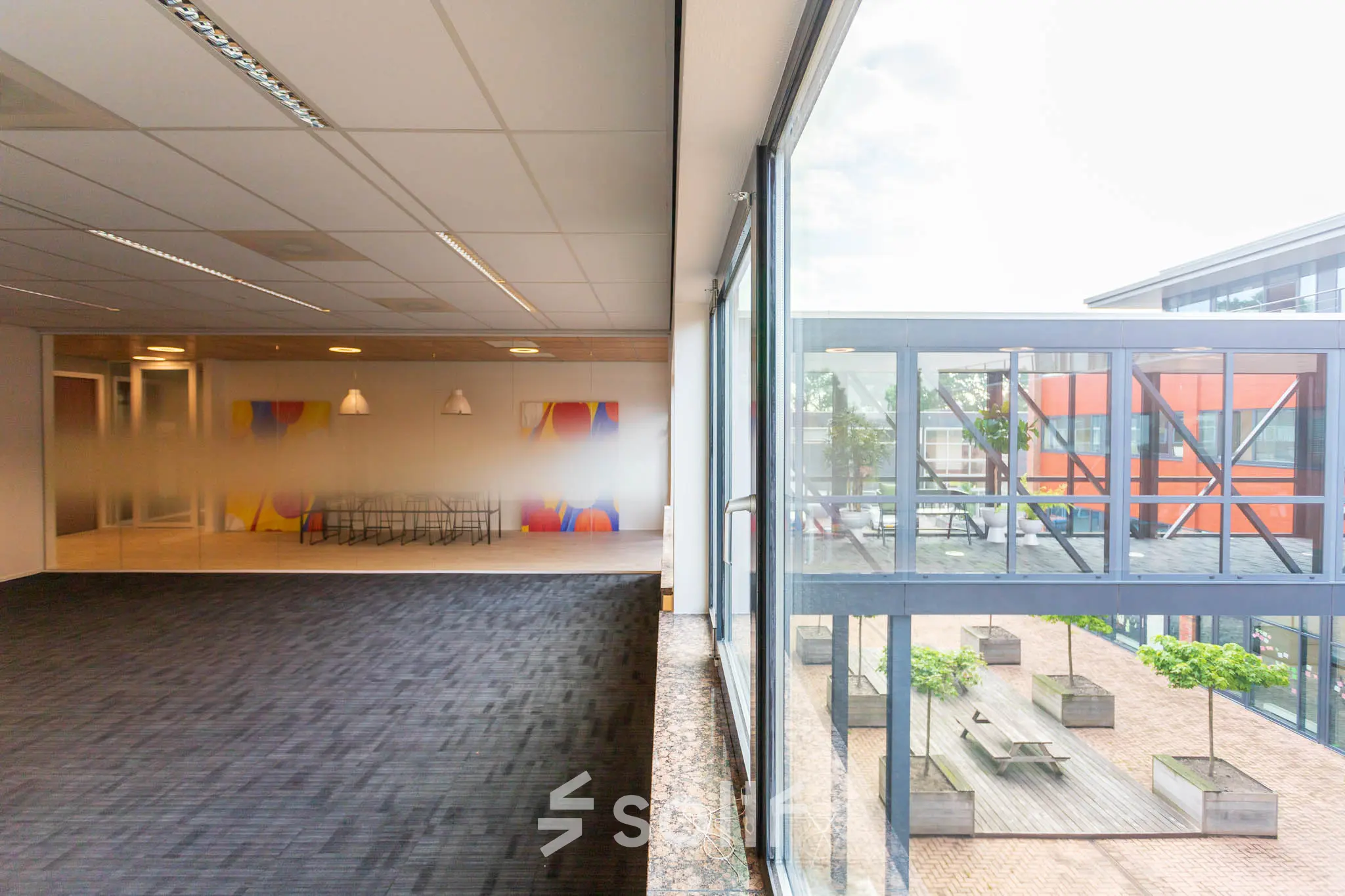 Kantoorruimte huren in Leiden op Pompoenweg 3 - 15, met grote ramen die uitzicht bieden op een binnenplaats. Het interieur bevat een vergaderruimte met kleurrijke achtergrond en een tapijtvloer.