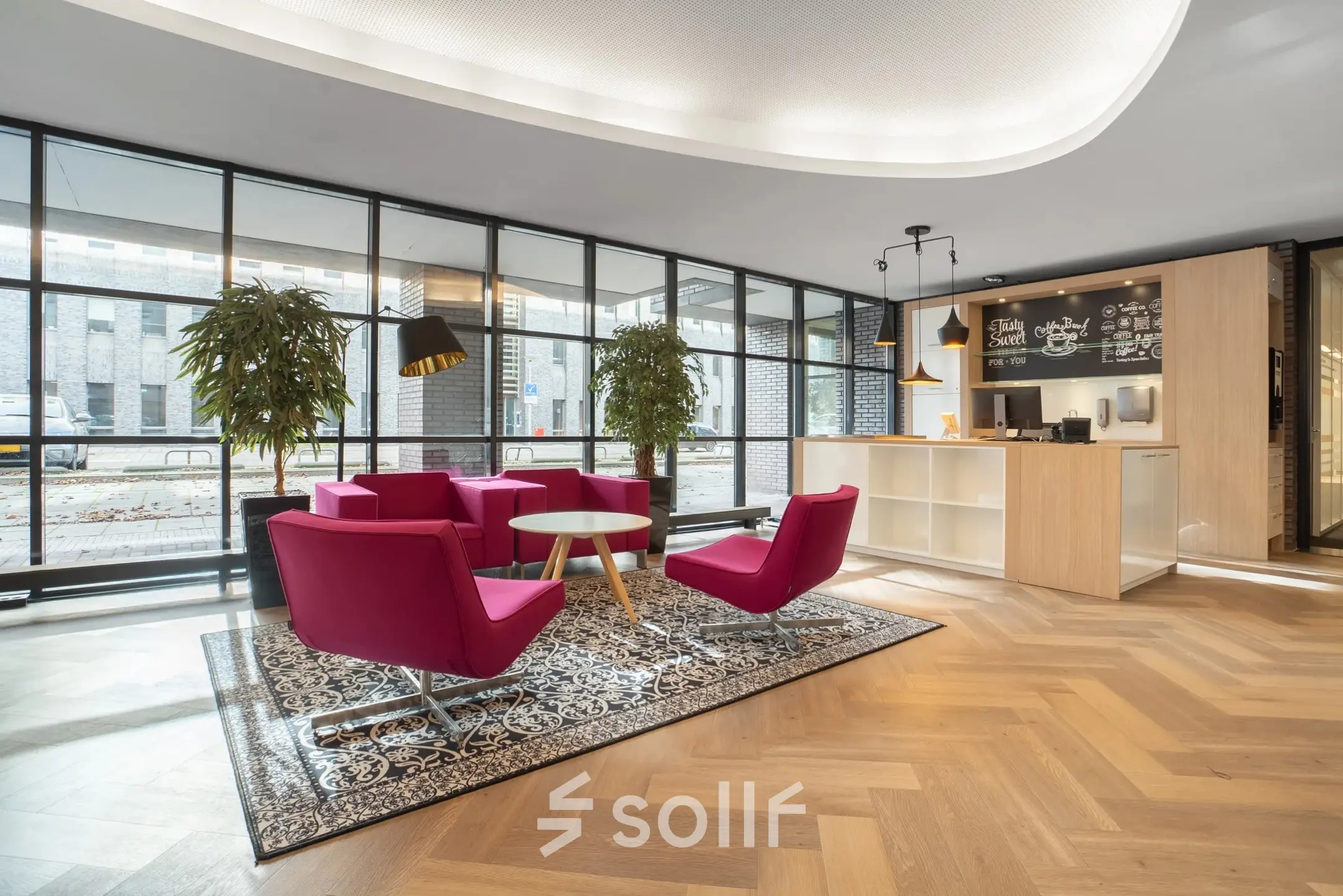 Moderne kantoorruimte met roze stoelen, een tapijt en een balie, geschikt voor kantoorruimte huren in Maastricht.