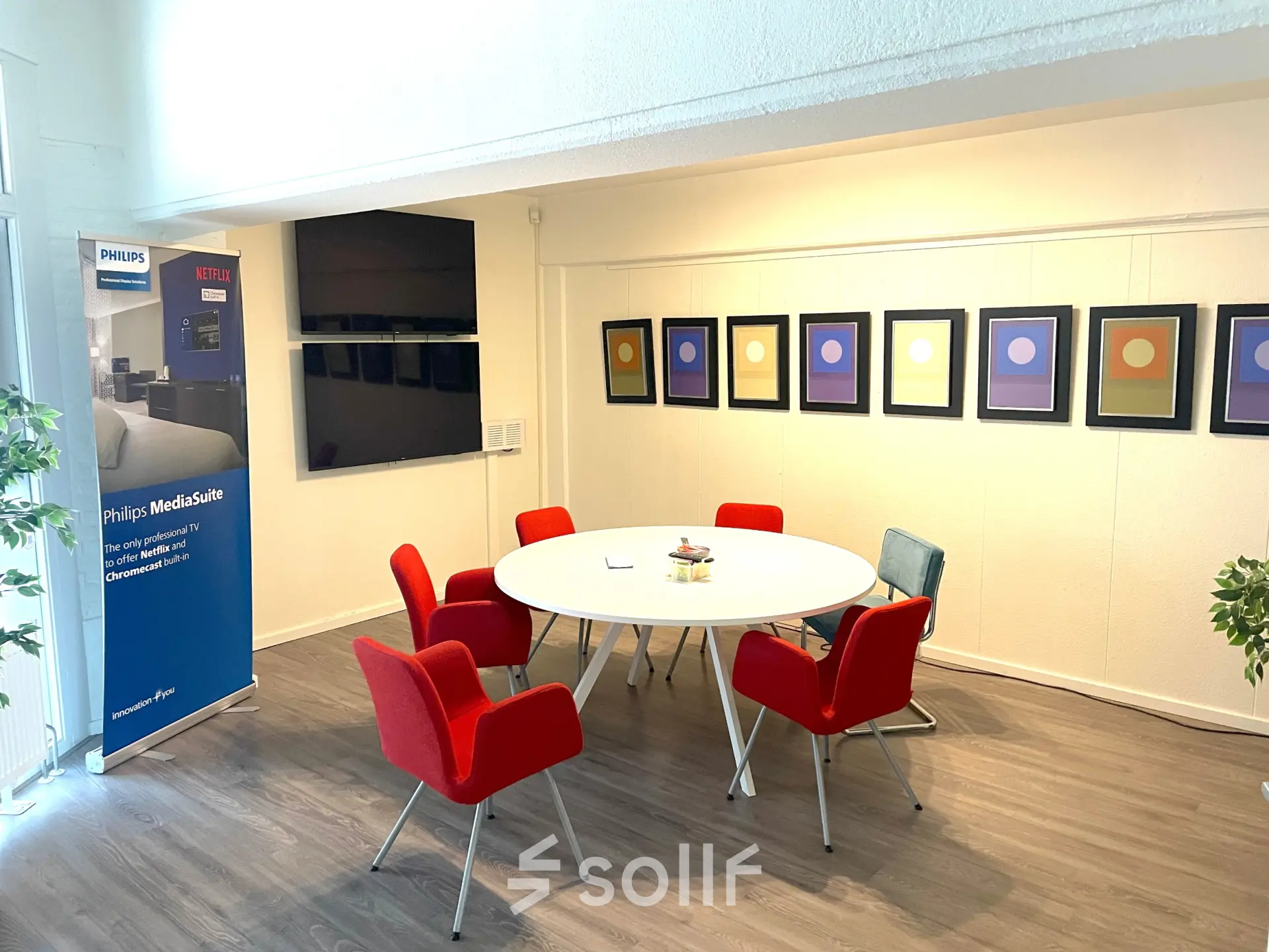 Vergaderruimte in kantoorpand op Wilhelminasingel 44-46 in Maastricht, met rode stoelen rond een witte tafel en kleurrijke kunst aan de muur. Ideaal voor kantoorruimte huren.