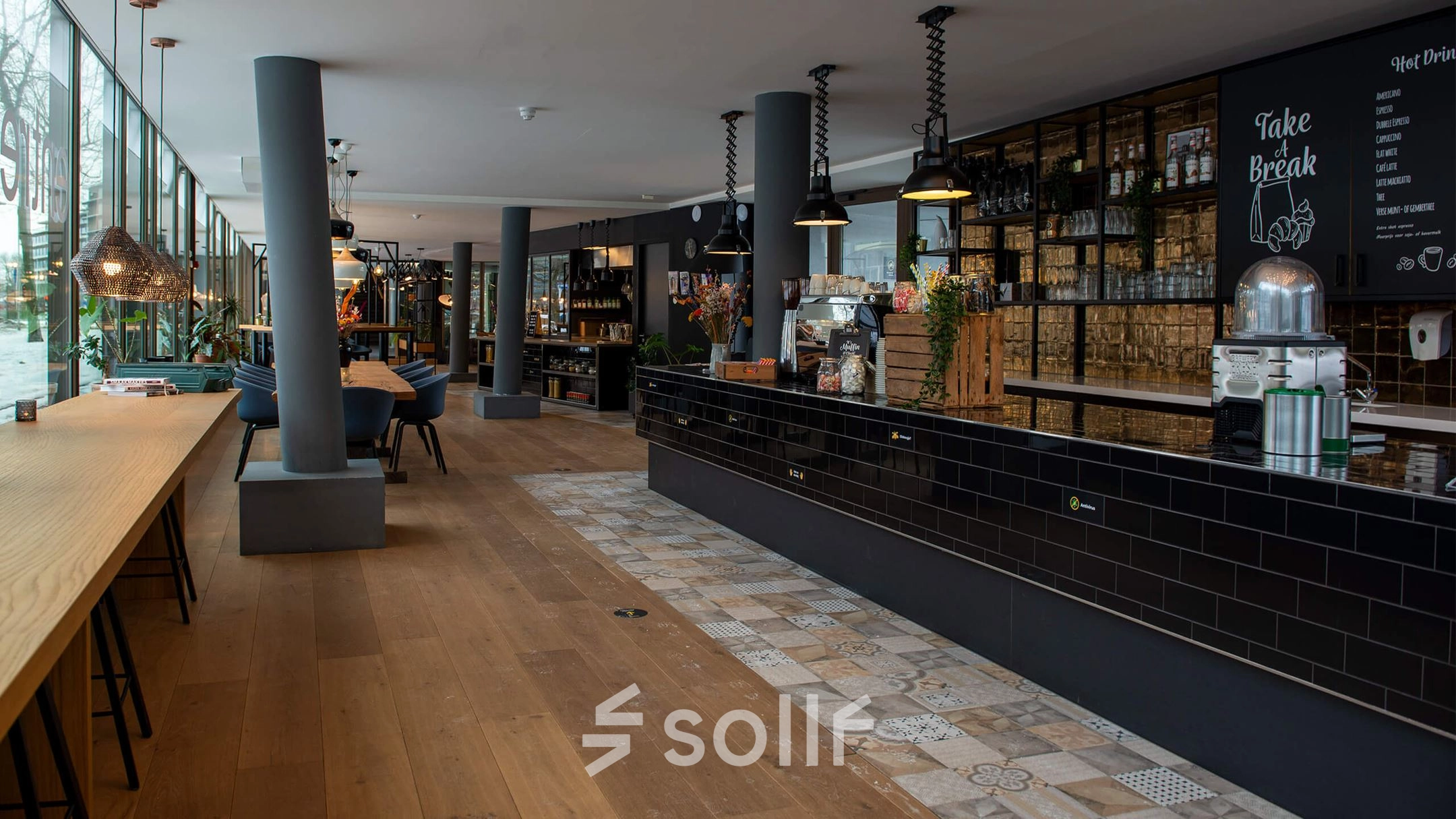 Moderne kantoorruimte in Meppel met lange tafels, sfeervolle verlichting en een stijlvolle zwarte balie, ideaal voor huur.