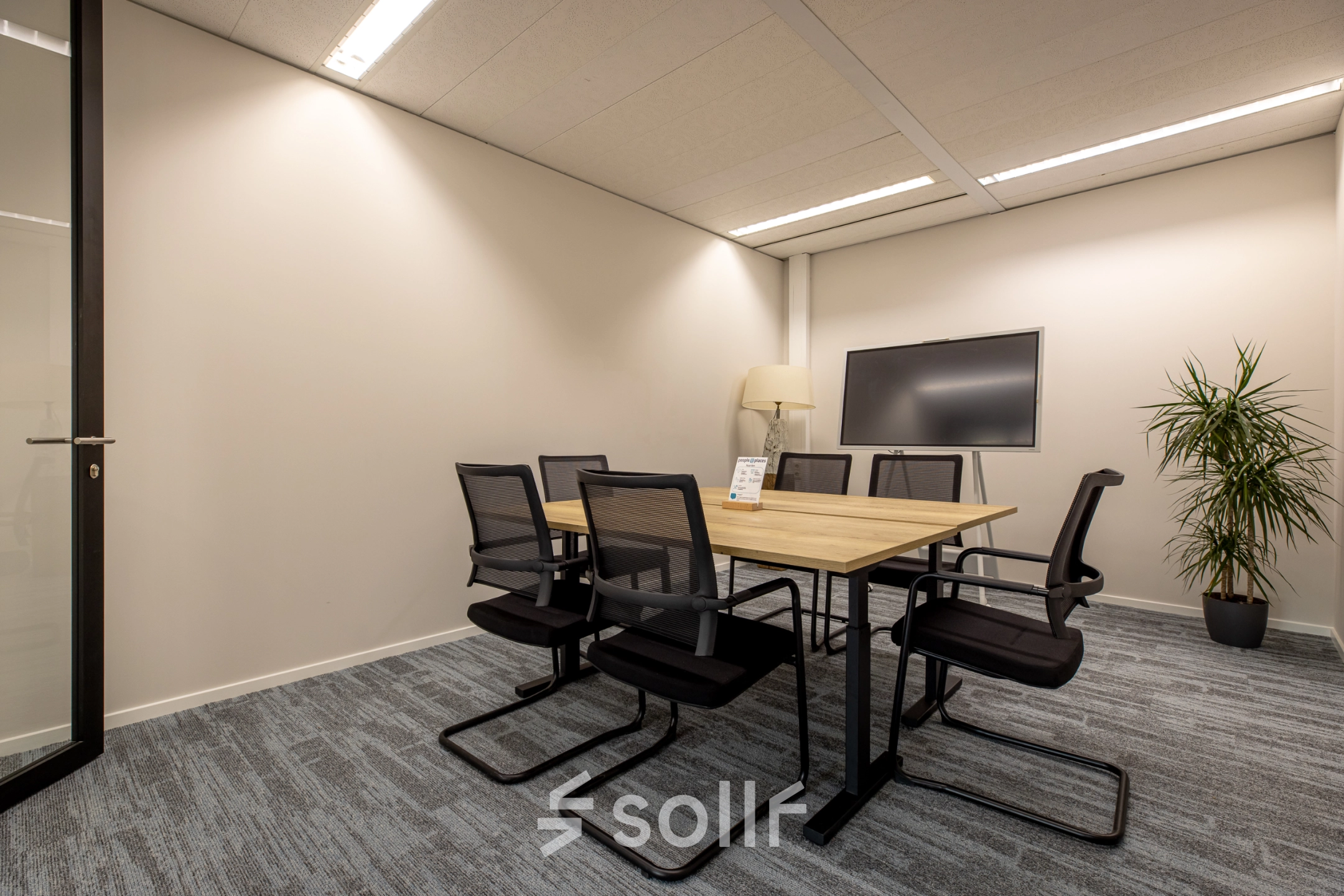 Moderne vergaderruimte in kantoorpand op Gooimeer 1, Naarden, met zes stoelen rond een houten tafel en een groot beeldscherm aan de muur. Ideaal voor bedrijven die kantoorruimte willen huren.