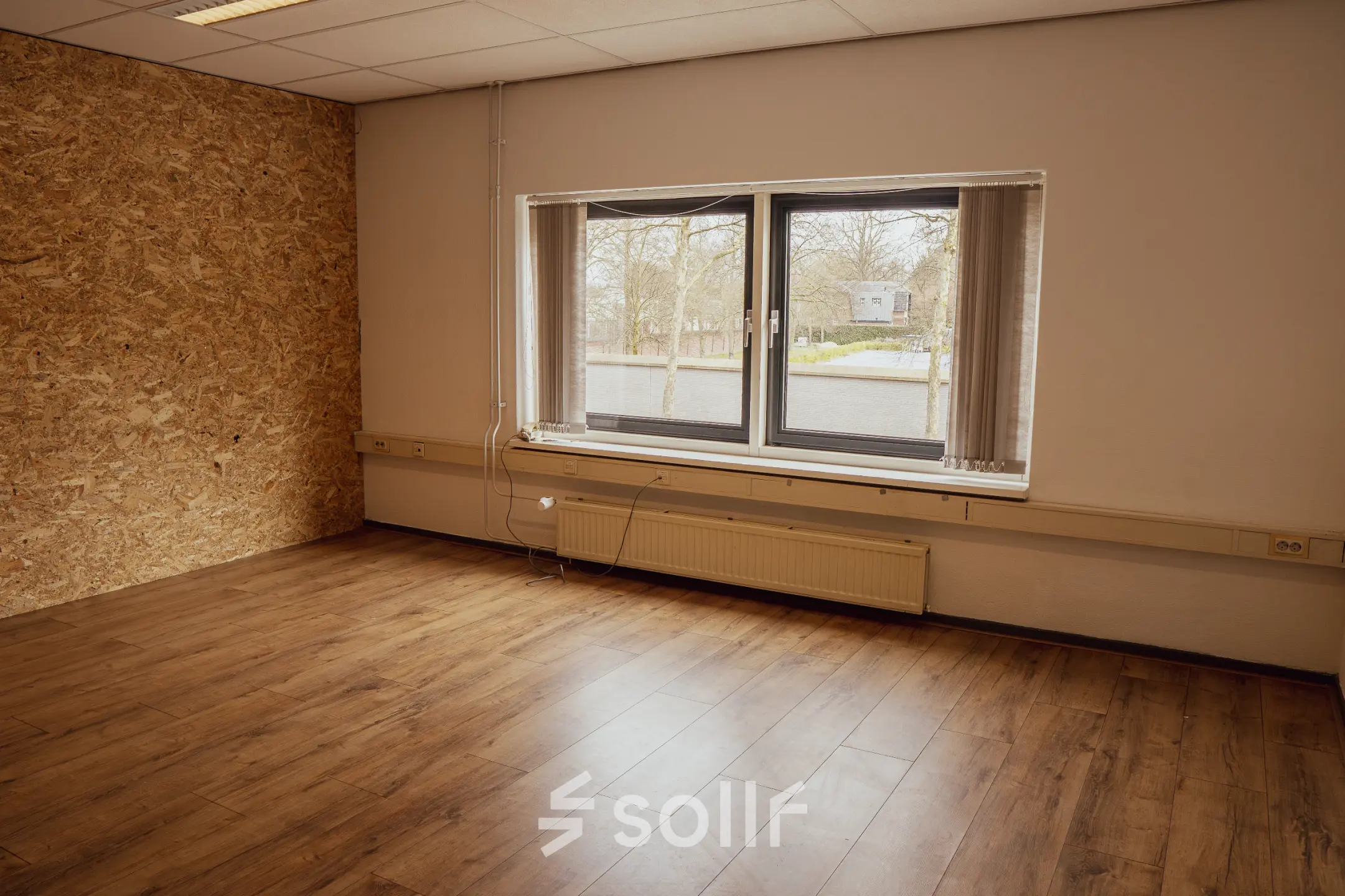 Lege kantoorruimte met houten vloer en groot raam met uitzicht op de straat, in een kantoorpand aan de Abdis van Thornstraat 74 in Oosterhout Nb.