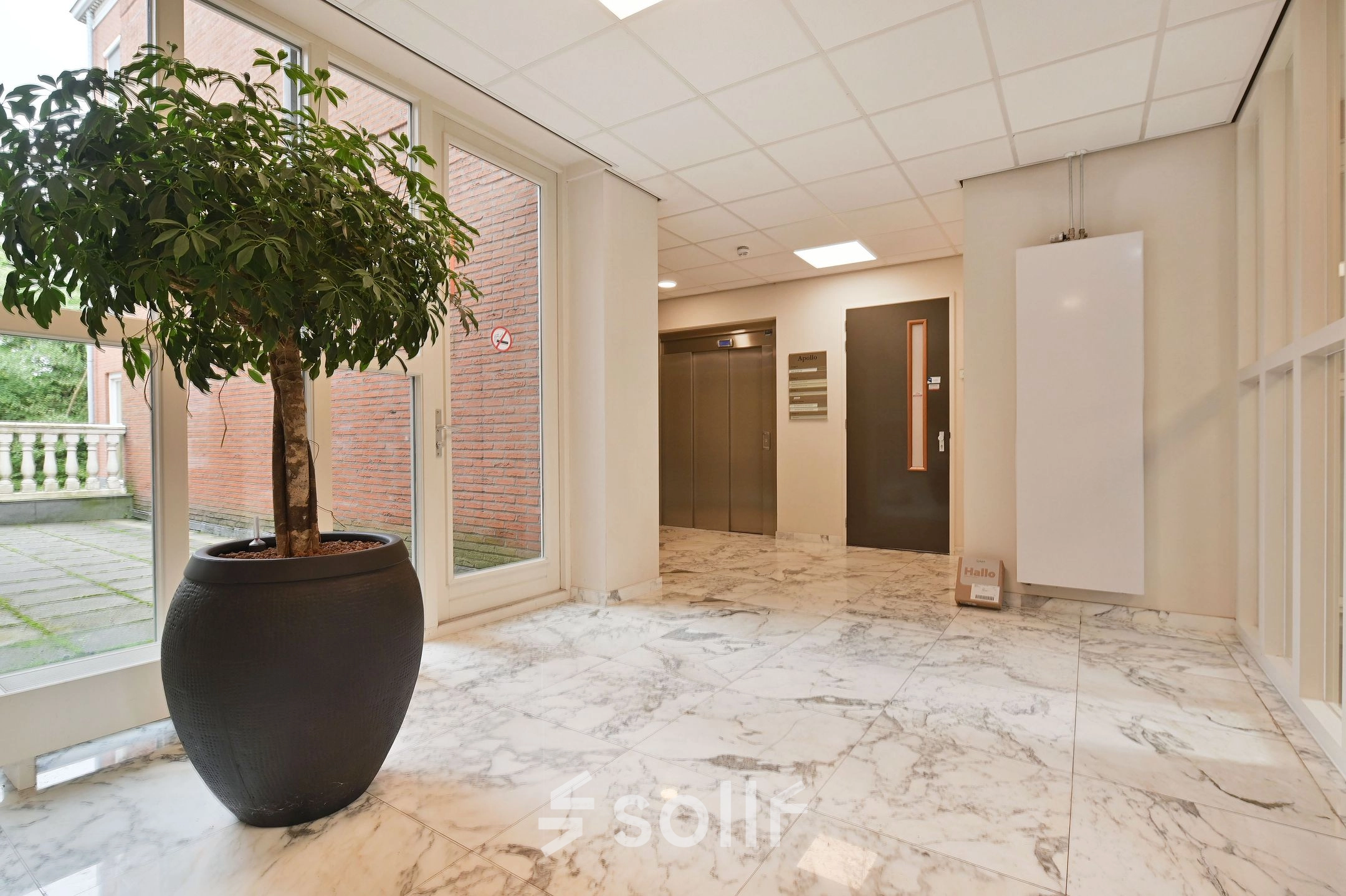 Entree van een kantoorpand aan de Laan van Vredenoord 17-19 in Rijswijk, met marmeren vloer en een grote plant naast de lift. Ideaal voor kantoorruimte huren.
