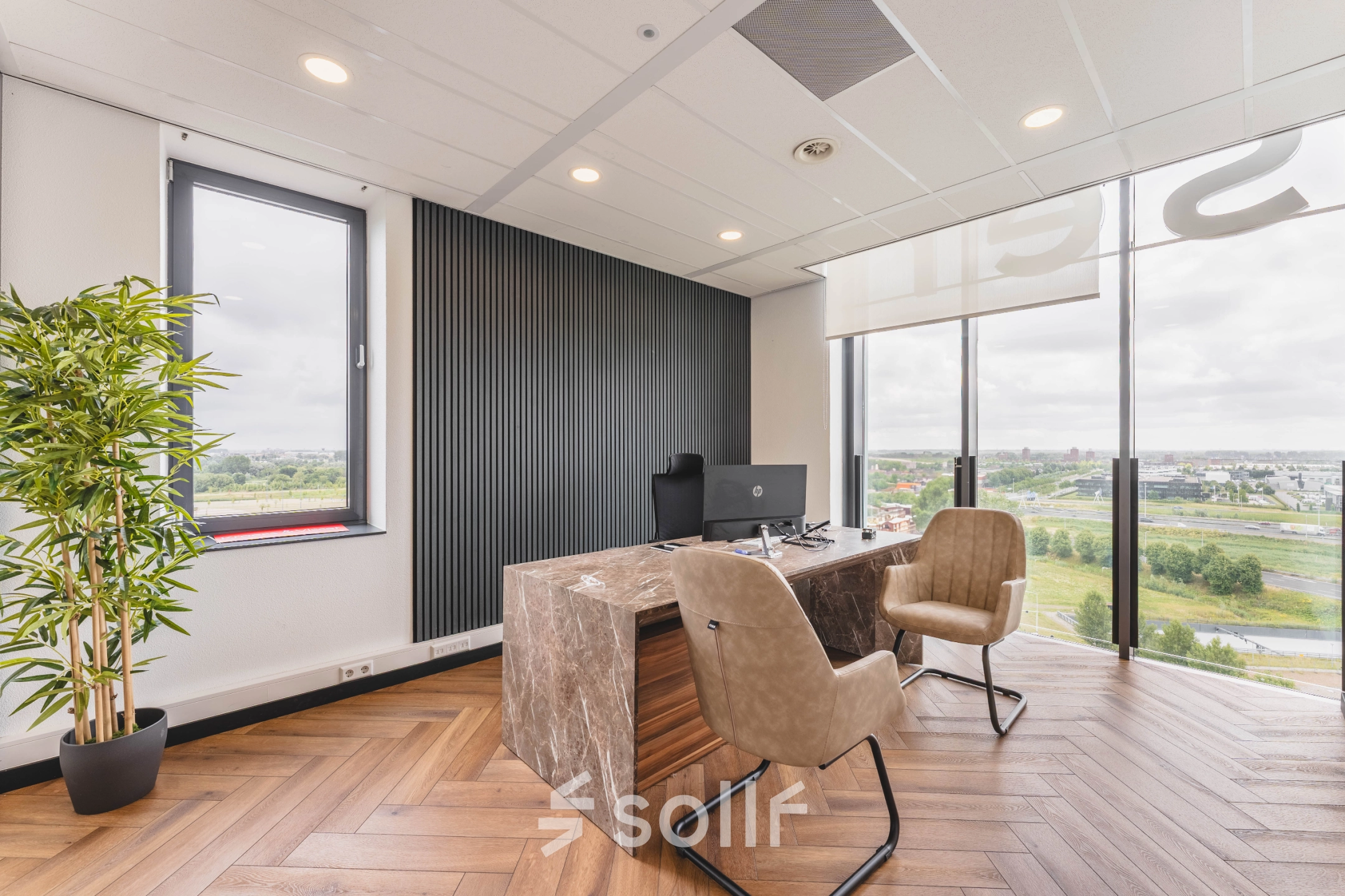 Kantoorruimte met houten vloer, marmeren bureau, comfortabele stoelen en uitzicht op Rijswijk. Geschikt voor werken en kantoorruimte huren.