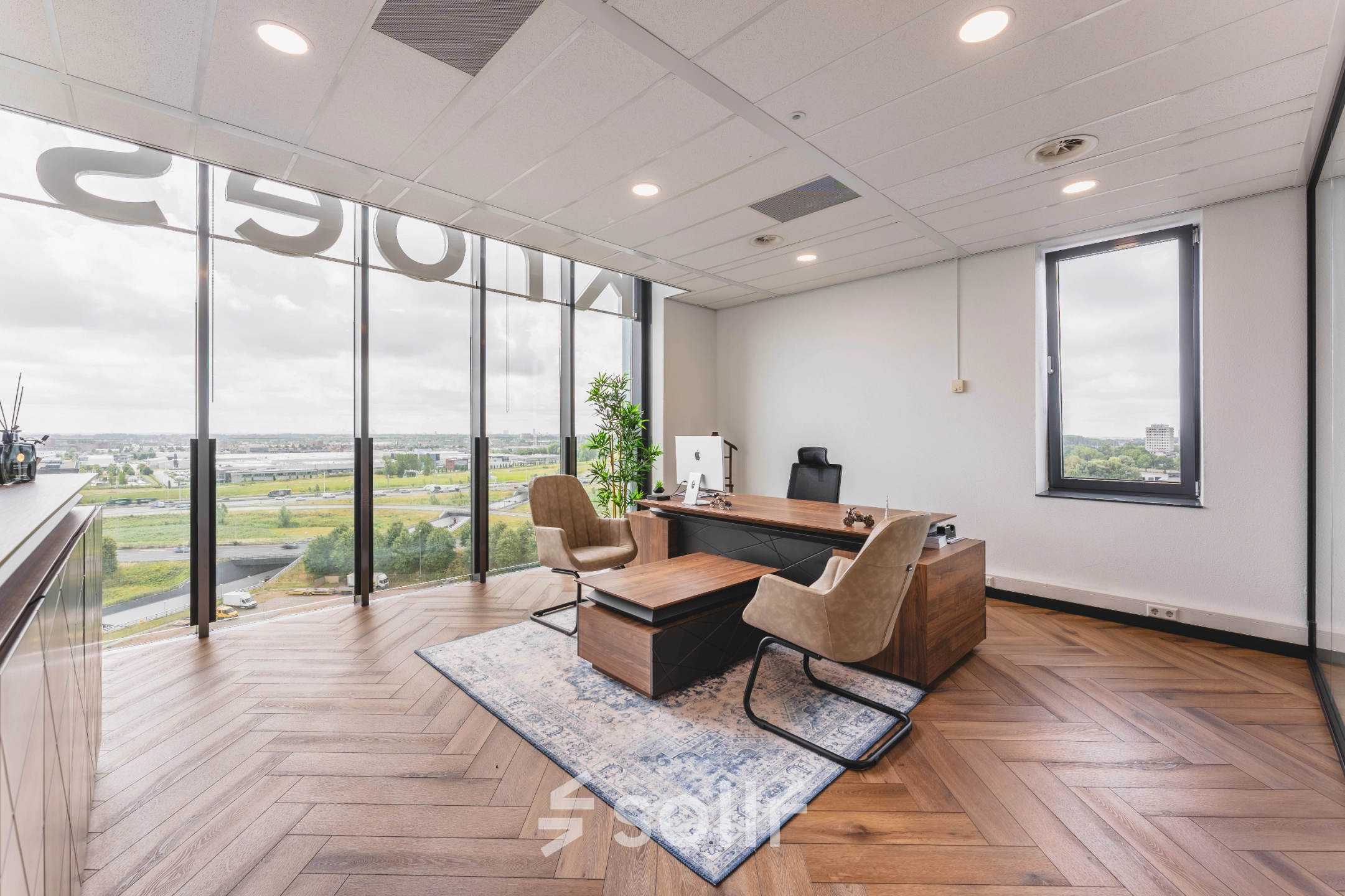 Moderne kantoorruimte in Rijswijk met groot raam, uitzicht over stad. Kantoorinrichting met bureau, stoelen en tapijt. Geschikt voor kantoorruimte huren.