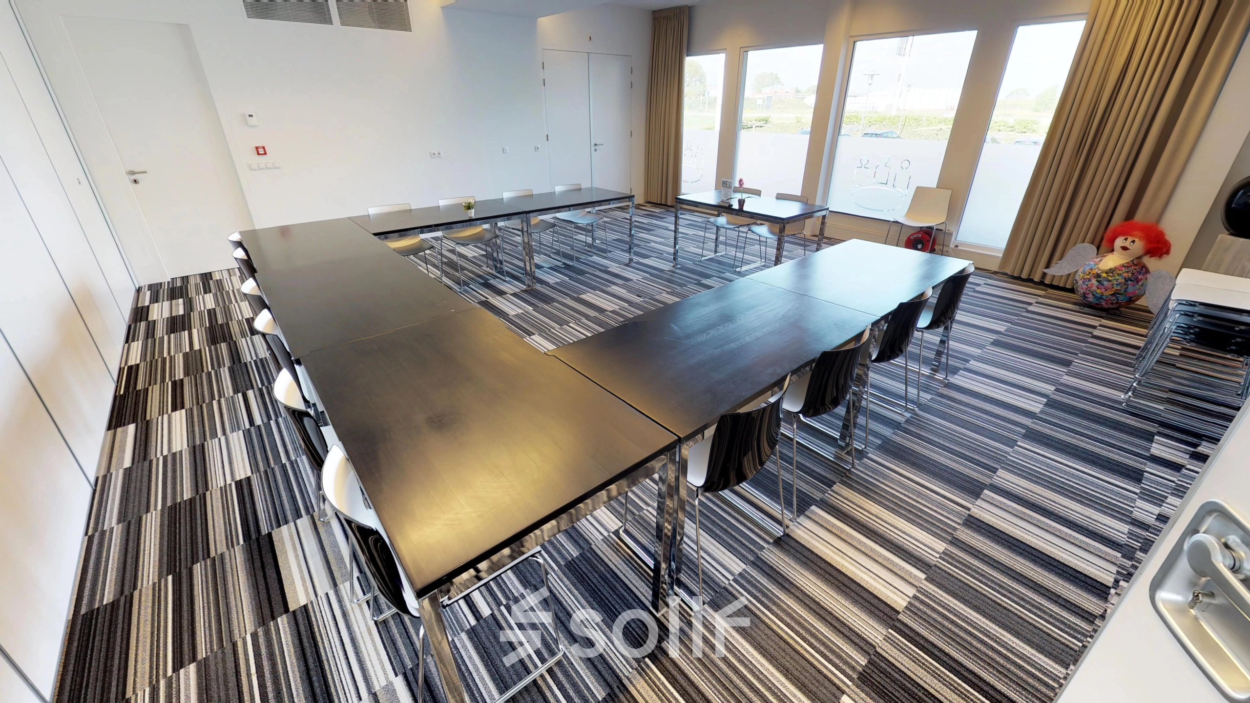 U-vormige vergaderruimte in Roermond met stijlvolle bureaus en stoelen, grote ramen zorgen voor veel natuurlijk licht. Kantoorruimte huren op Boven de Wolfskuil 3 biedt een moderne setting voor zakelijke bijeenkomsten.