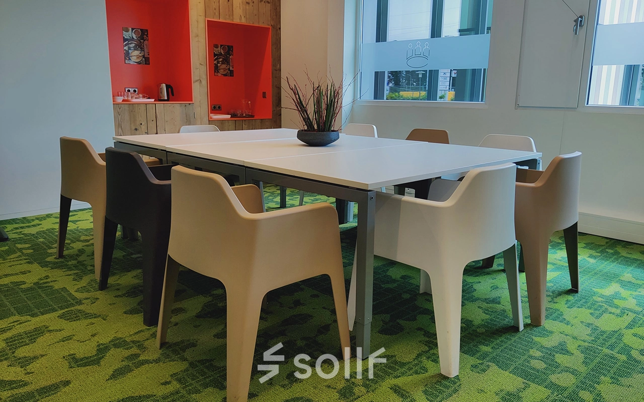 Een moderne kantooruimte met een lange tafel omringd door stoelen in een kleurrijke setting op Boven de Wolfskuil 3, Roermond, geschikt voor vergaderingen of als werkplek te huur.