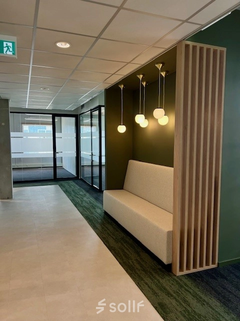 Entree van een modern kantoorpand op Bahialaan 100 in Rotterdam Brainpark, met stijlvolle verlichting en een bank tegen een groene muur. Ideale kantoorruimte huren in Rotterdam.