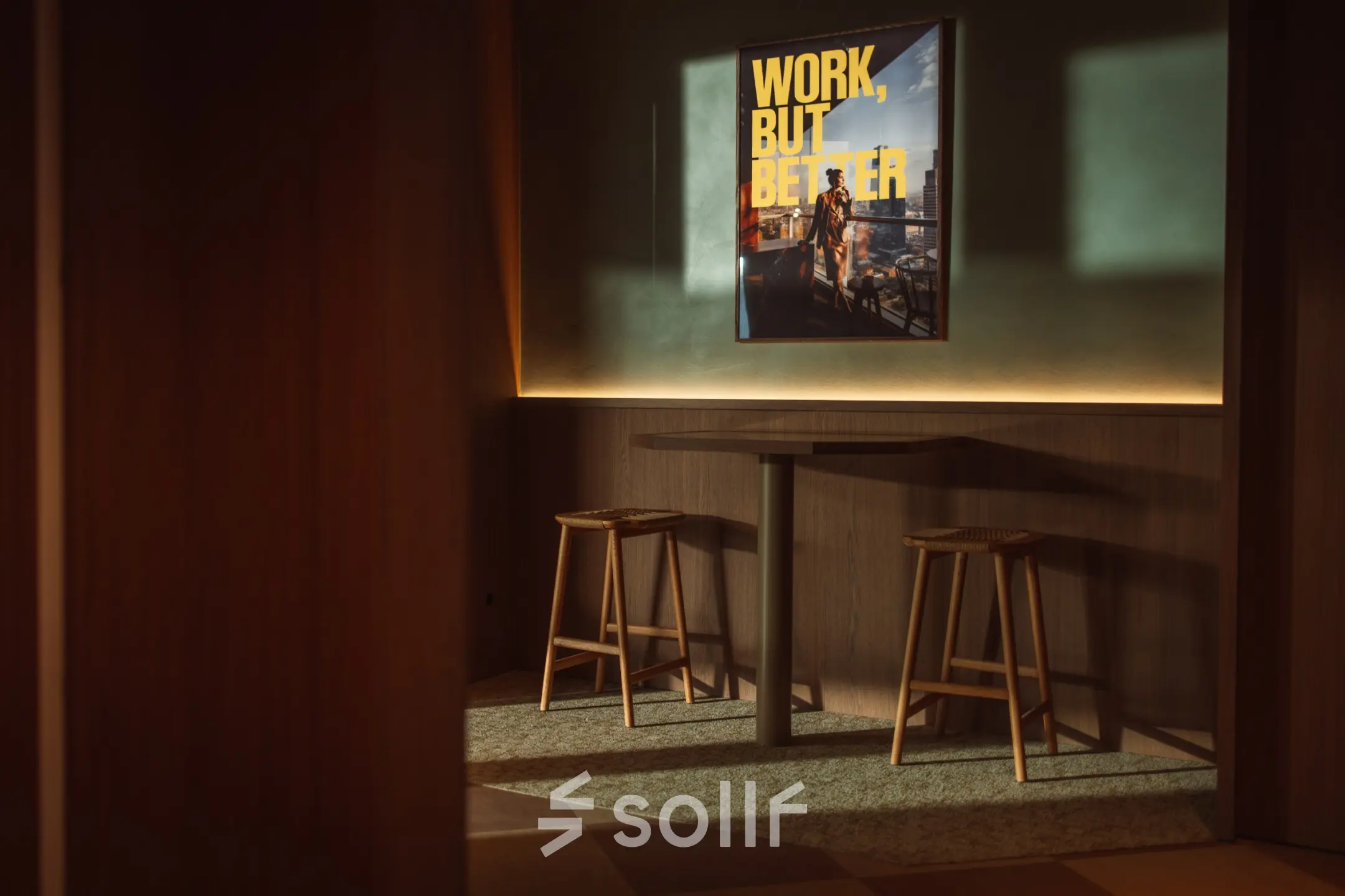 Gezellige zitplek met houten tafel en krukken, omringd door warme verlichting in een kantoorpand aan de Coolsingel 139, Rotterdam Centrum. Poster met inspirerende tekst aan de muur.