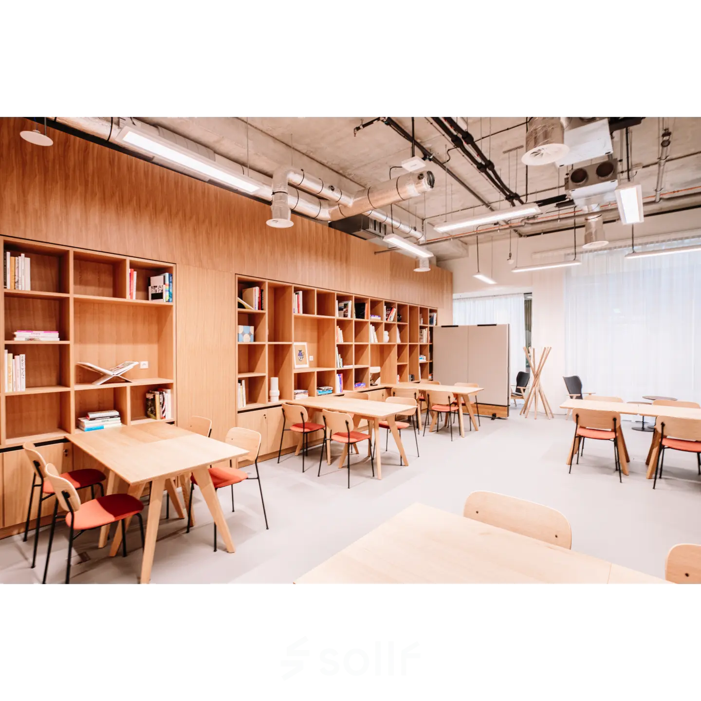 Moderne kantoorruimte in Rotterdam Centrum met houten tafels en stoelen, geschikt voor verhuur. De ruimte heeft een open indeling met boekenplanken tegen de muur, ideaal voor creatieve werkplekken.