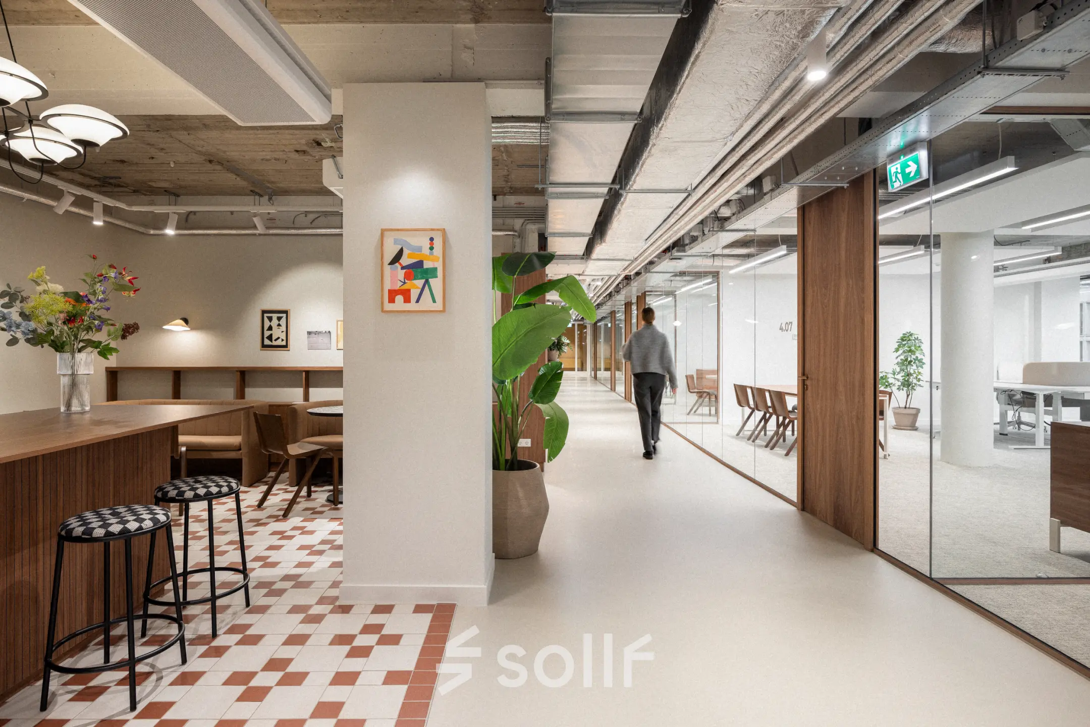 Modern kantoorpand op Stadhuisplein 9-23, Rotterdam Centrum met open werkruimtes en glazen wanden, ideaal voor kantoorruimte huren. Een persoon loopt langs bureaus in een lichte, strak ingerichte omgeving.