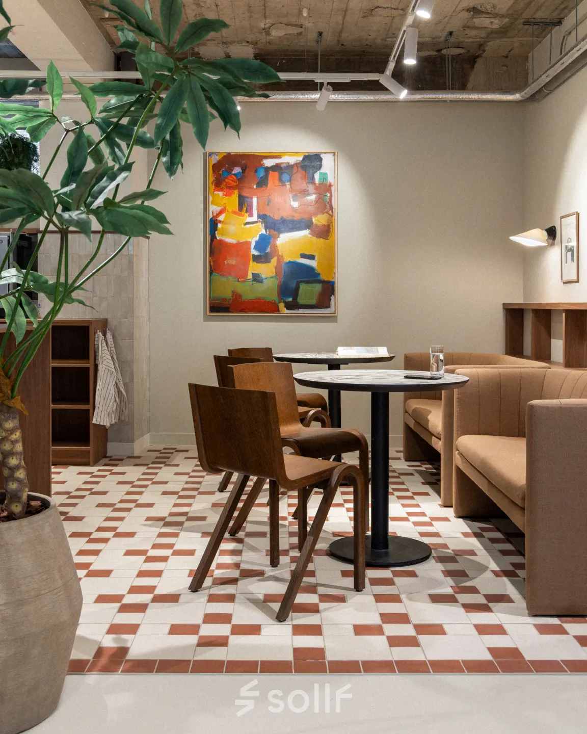 Moderne kantoorruimte in Rotterdam Centrum met gezellige zithoek, hoog plafond, kleurrijk schilderij en stijlvolle meubels. Ideale plek voor informeel overleg of ontspannen pauze.