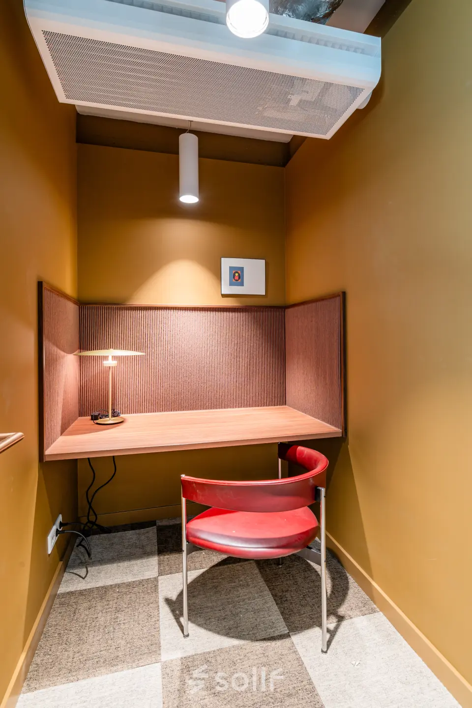 Kantoorruimte huren in Rotterdam Centrum op Stadhuisplein 9-23. Geisoleerde werkplek met een rode stoel en bureau, omgeven door warme okerkleurige muren. Ideaal voor geconcentreerd werken in het kantoorpand.