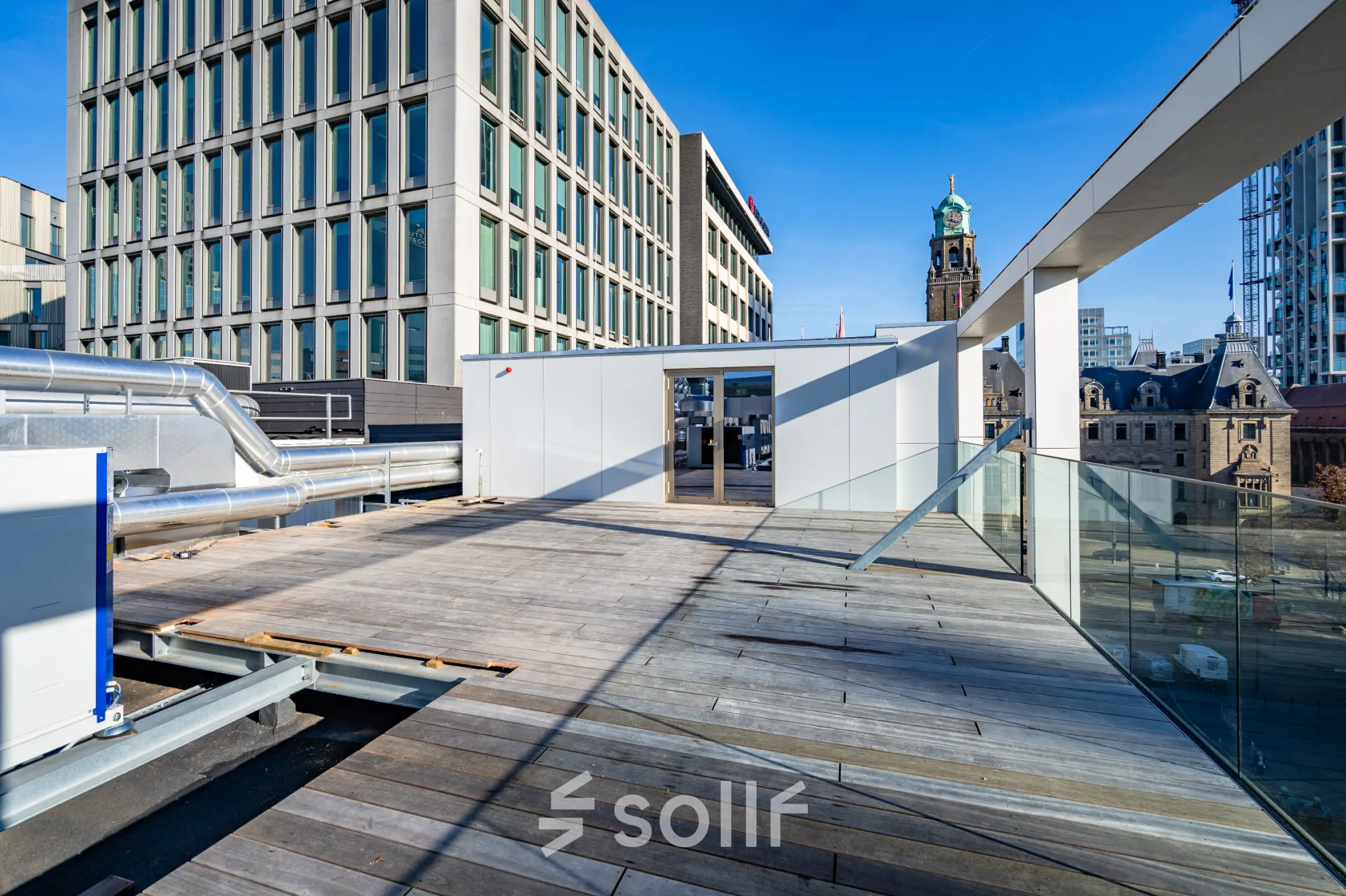 Een ruim dakterras met houten vloer en glazen balustrades op Stadhuisplein 9-23, Rotterdam Centrum. Geschikt om kantoorruimte te huren of als ontspanningsruimte voor huurders van het kantoorpand.