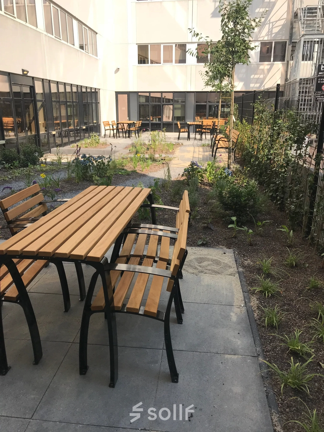 Buitenruimte van een kantoorpand met houten tafels en banken, omlijst door groen, gelegen op Westblaak 180 in Rotterdam Centrum.