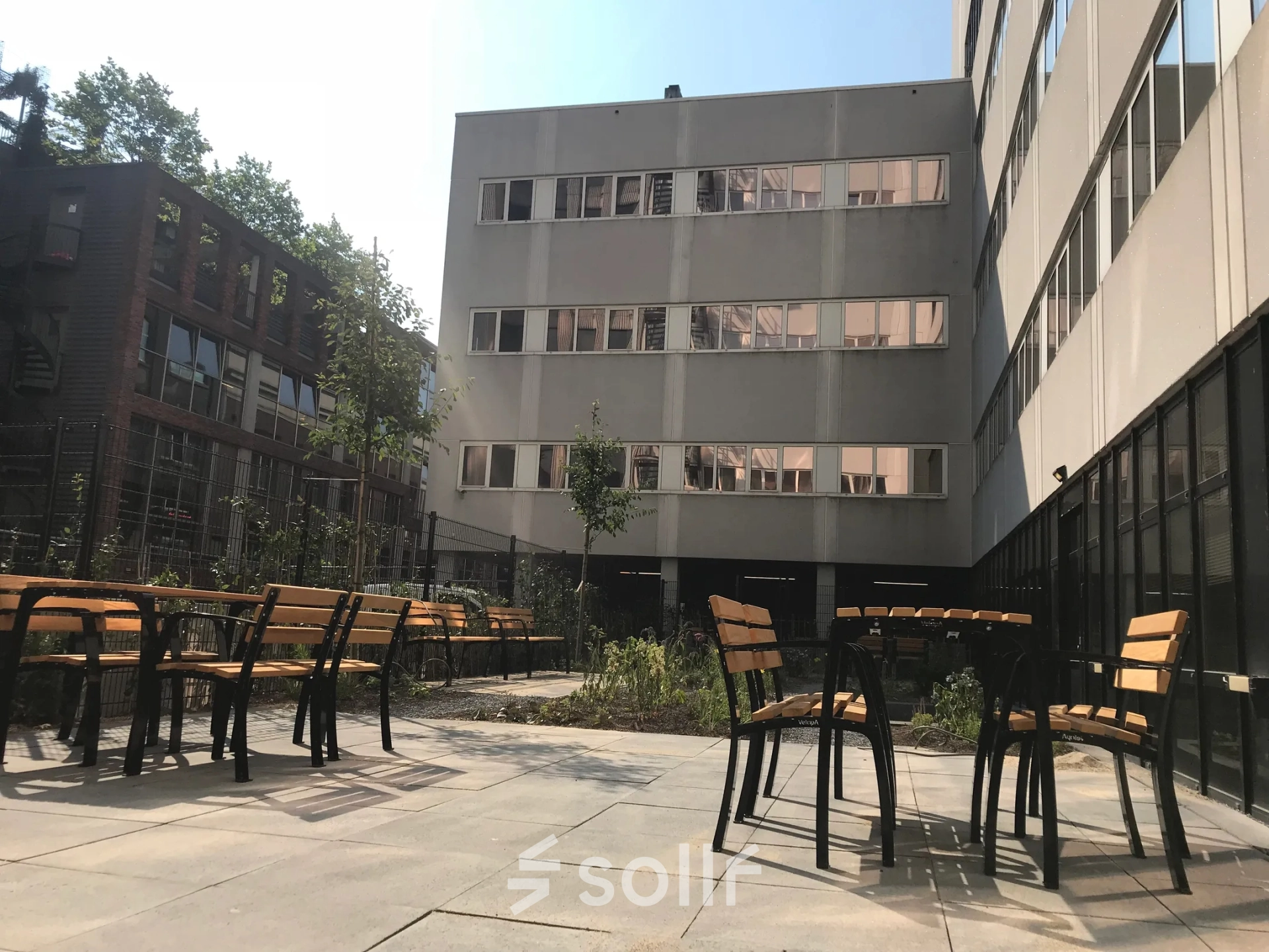 Buitenaanzicht van kantoorpand Westblaak 180 in Rotterdam Centrum, met moderne architectuur en betegeld terras met houten tafels en stoelen.
