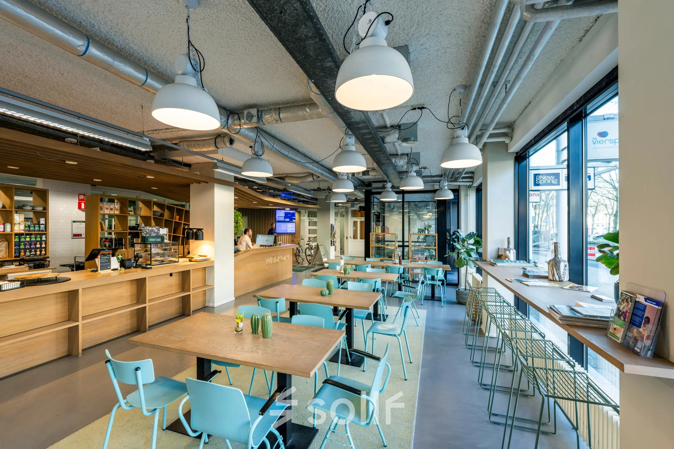Moderne en lichte kantoorruimte op Westblaak 180 in Rotterdam Centrum, geschikt voor verhuur. De ruimte heeft een open indeling met houten tafels en blauwe stoelen neergezet in een café-achtige opstelling.