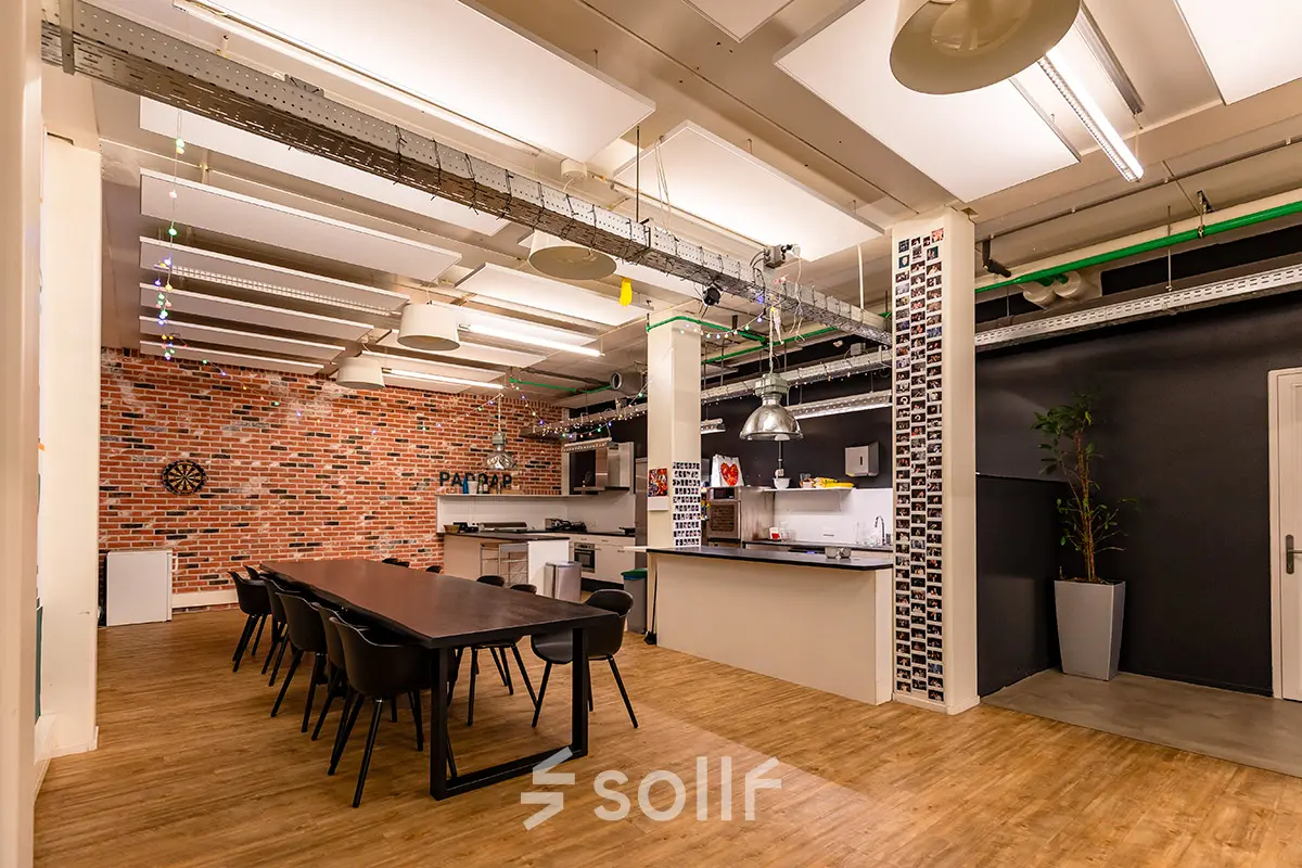 Moderne kantoorruimte huren in Rotterdam Delfshaven, Kratonkade 7-27. Een open ruimte met een keuken en een lange tafel, perfect voor vergaderingen en samenwerking.