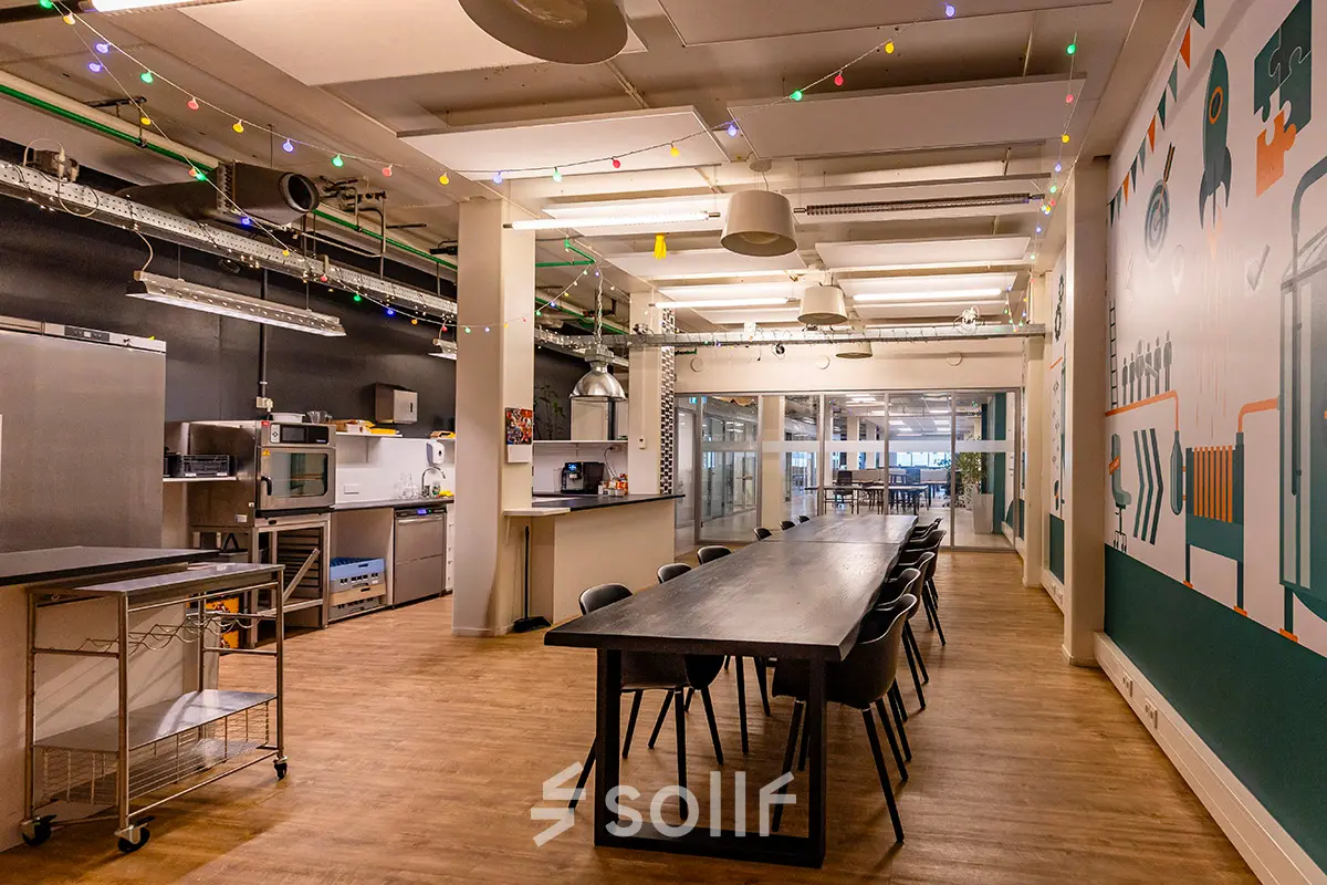 Kantoorruimte huren op Kratonkade 7-27 in Rotterdam Delfshaven met lange tafel, stoelen, moderne keukenfaciliteiten en kleurrijke verlichting. Ideaal voor samenwerking en creatieve projecten.