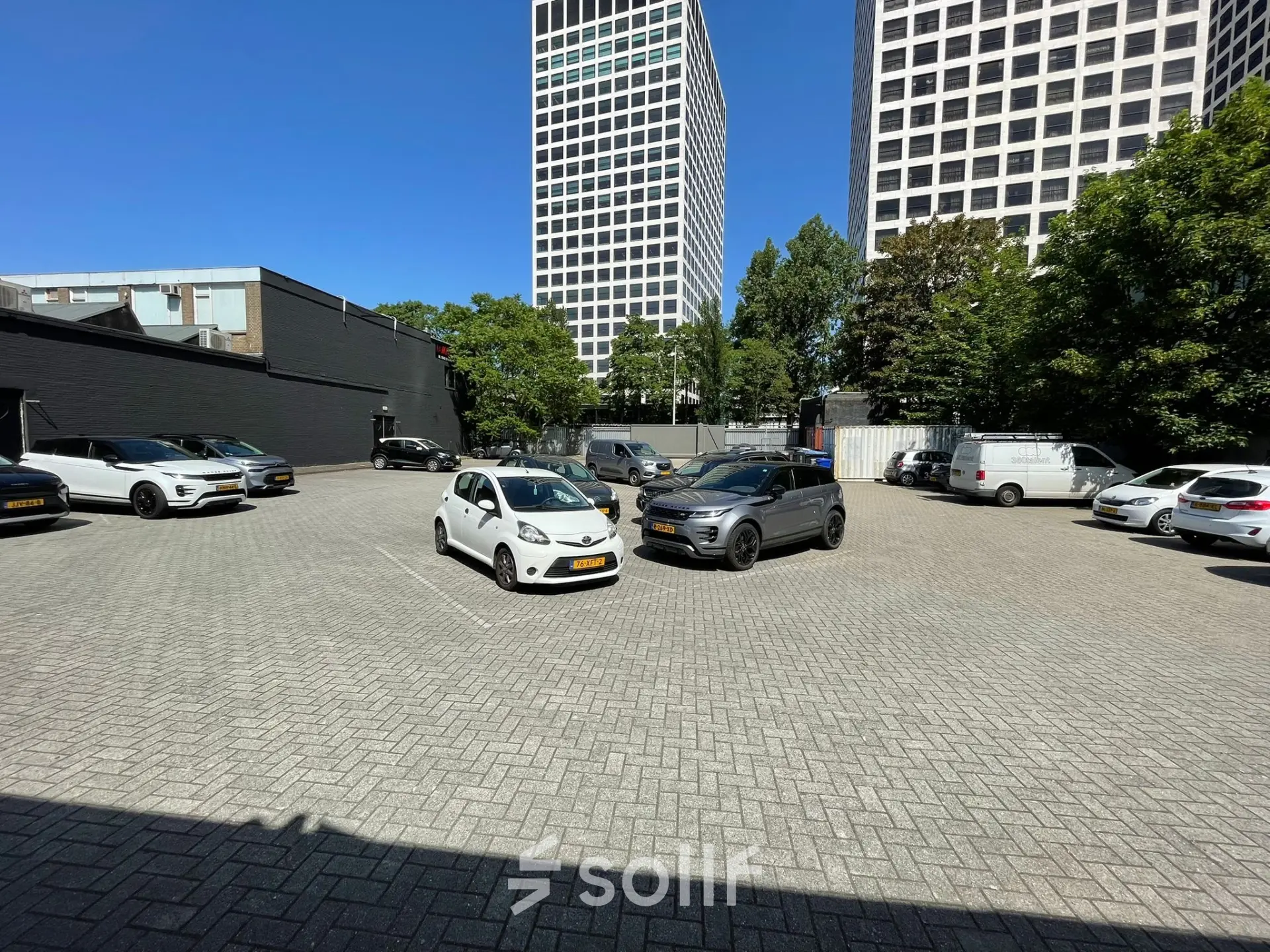 Parkeerplaats naast kantoorpand op Van Helmontstraat 17-23 in Rotterdam Delfshaven, met geparkeerde auto's en omringende hoge gebouwen.