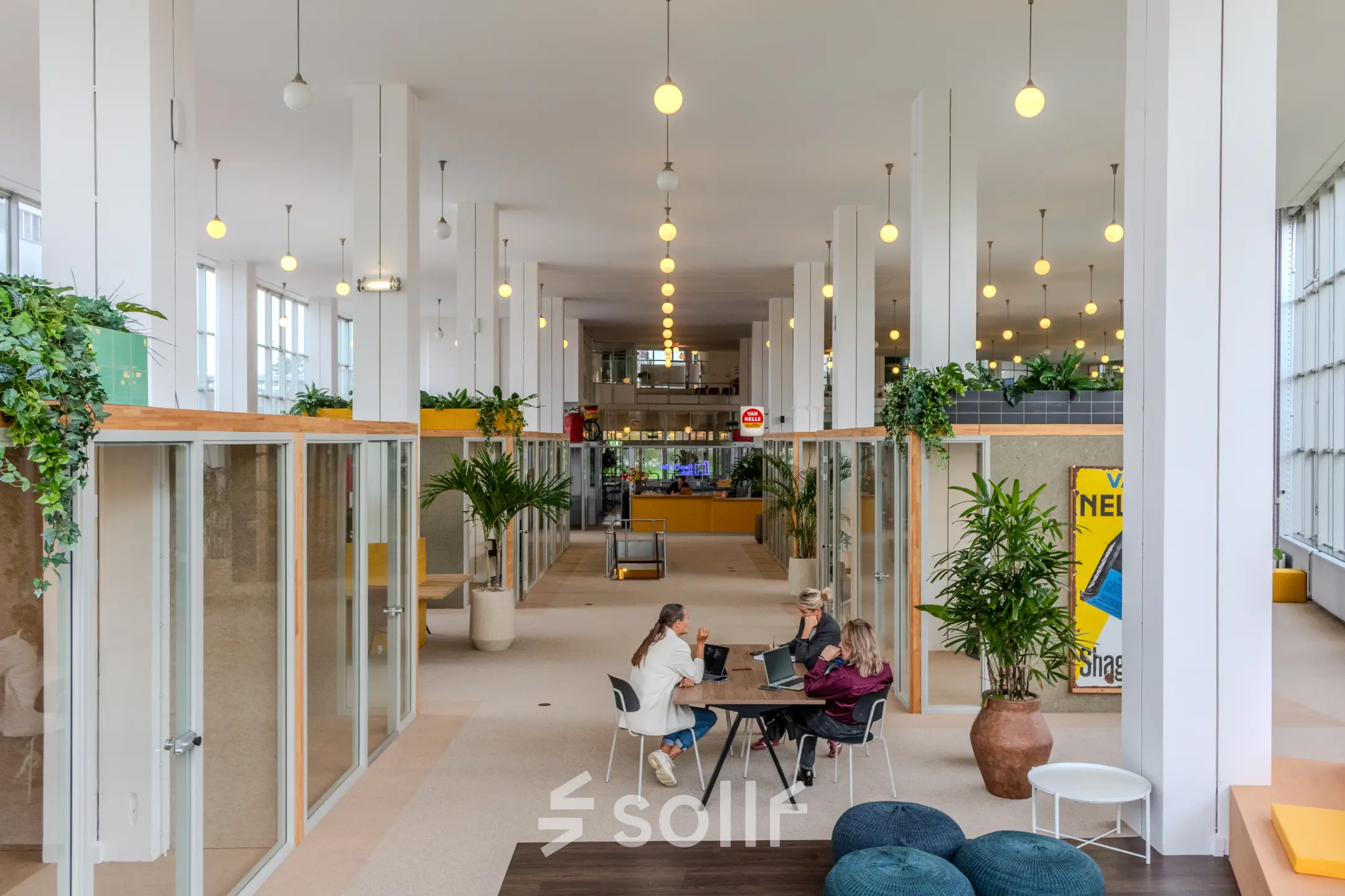Kantoorruimte huren op Van Nelleweg 1 in Rotterdam Delfshaven met moderne werkplekken, veel licht en planten. Vier personen aan een tafel voeren zakelijke activiteiten uit in een ruim kantoorpand.