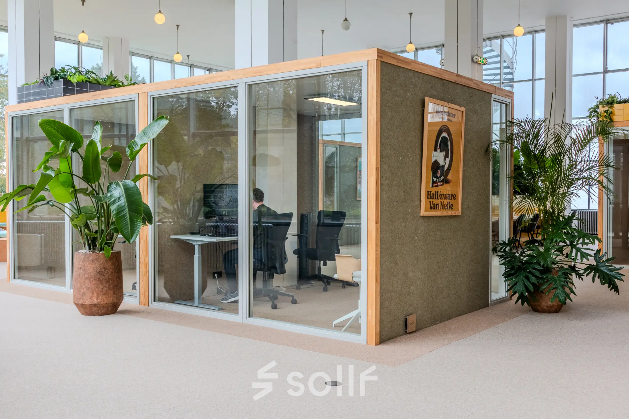 Moderne kantoorruimte te huur aan Van Nelleweg 1 in Rotterdam Delfshaven, ingericht met glazen wanden, enkele planten en een werkplek met een persoon bezig aan een computer.