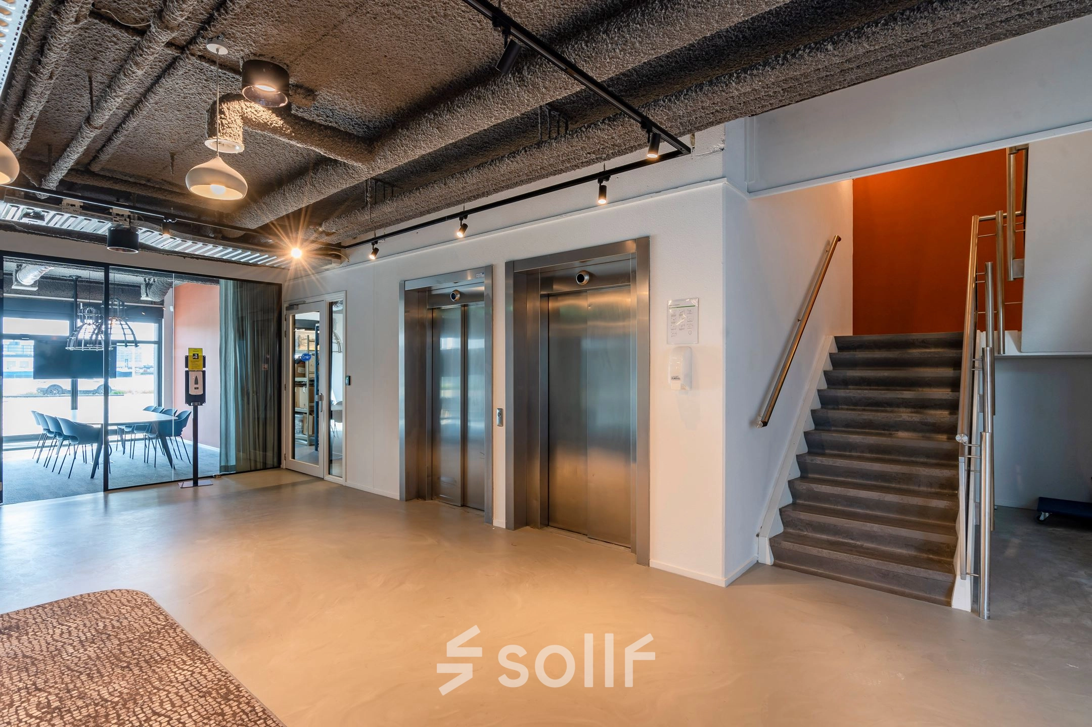 Een moderne kantoorruimte met liftlobby in het kantoorpand aan de Waalhaven O.z. 85, Rotterdam Waalhaven. Twee liften en een trap naast een zithoek met uitzicht op andere kantoren.