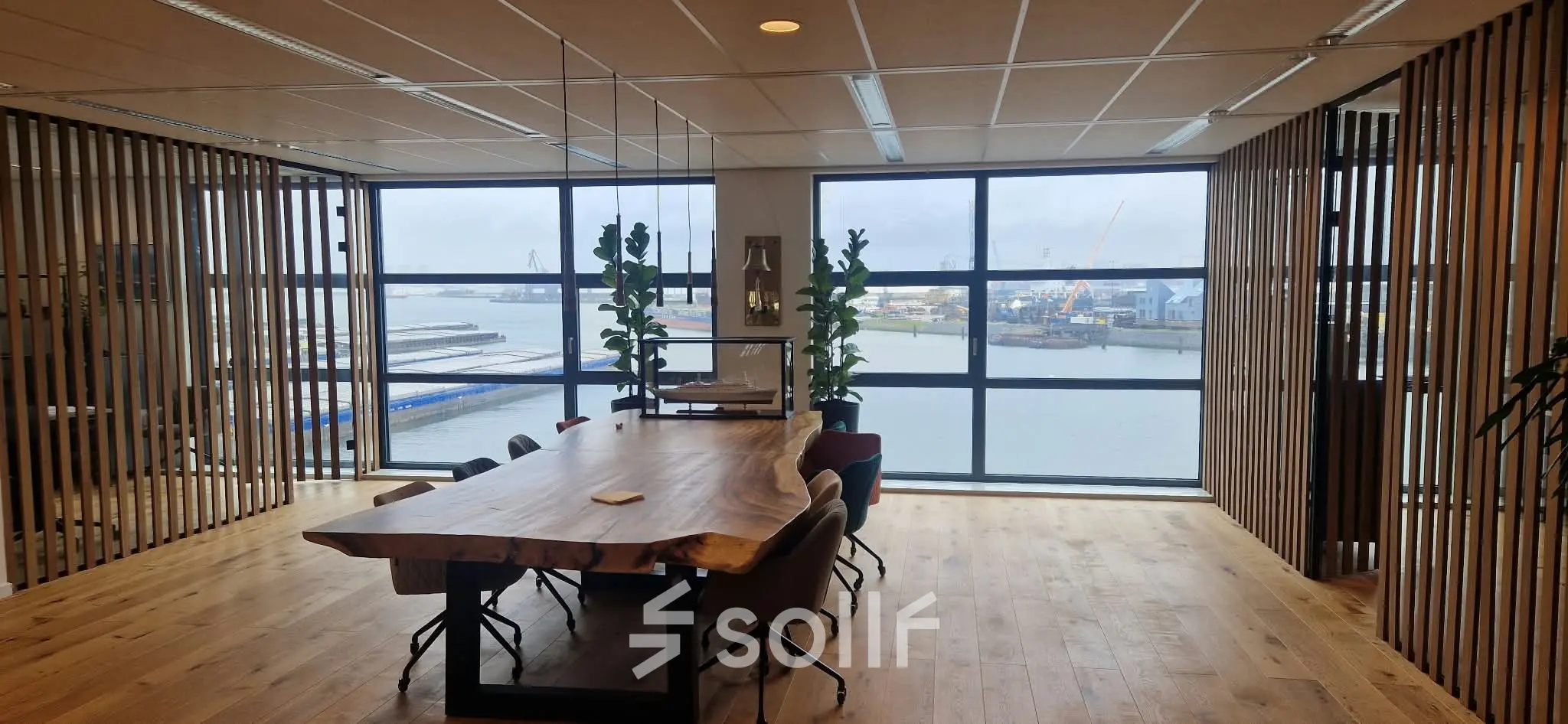 Vergaderruimte met houten tafel en stoelen, grote ramen met uitzicht op de haven, geschikt voor kantoorruimte huren in Rotterdam Waalhaven.