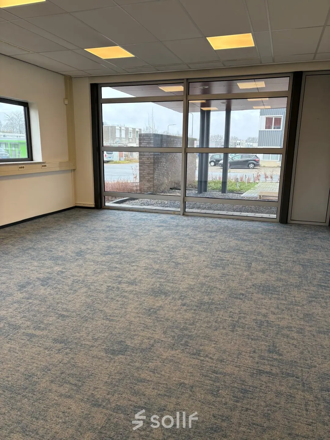 Lege kantoorruimte met grote ramen en blauw tapijt op Fischerpad 106, Sittard, beschikbaar om te huren.