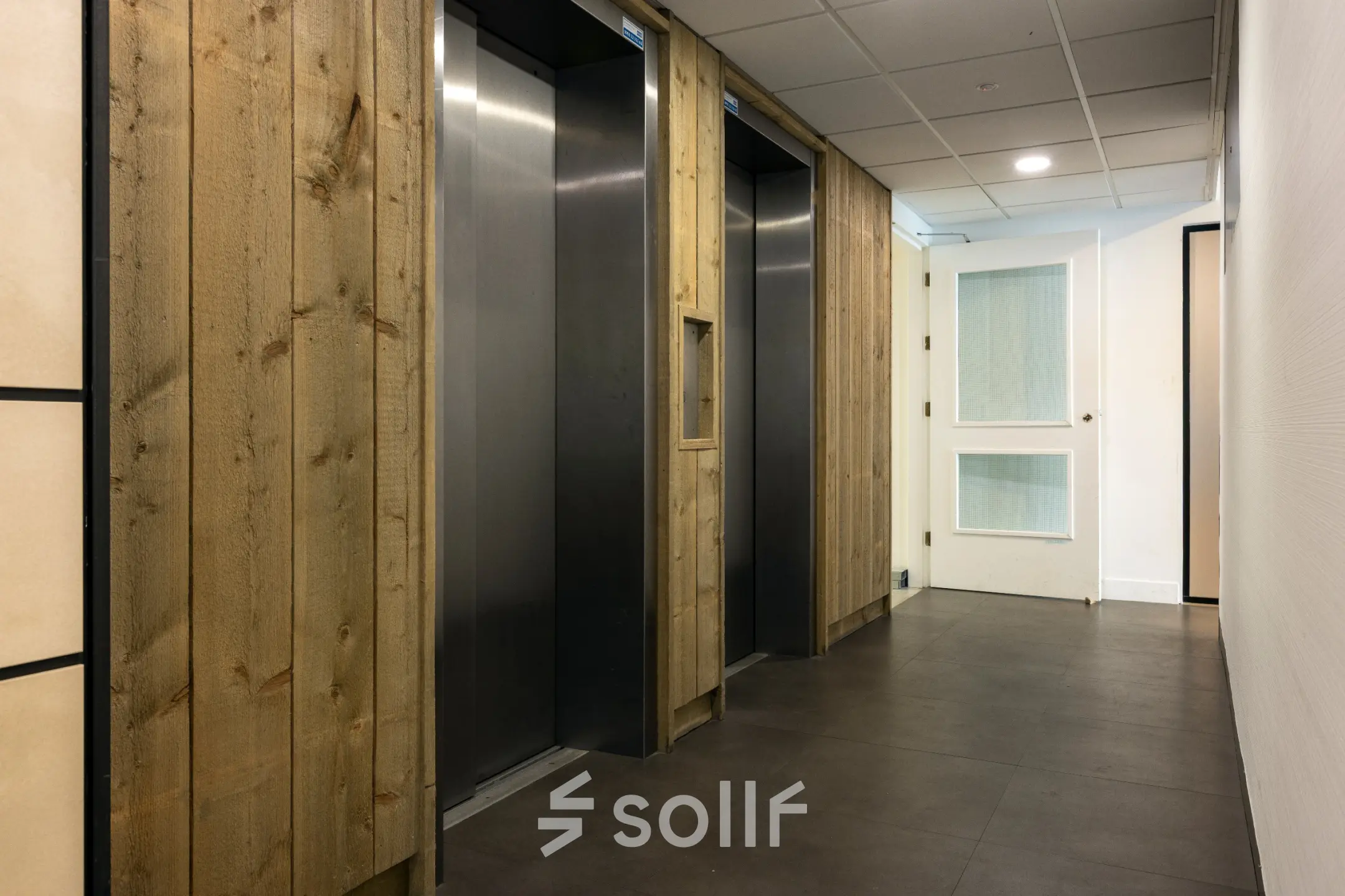 Gang met liftdeuren en houten accenten in een kantoorpand aan de Curieweg 9, Spijkenisse.