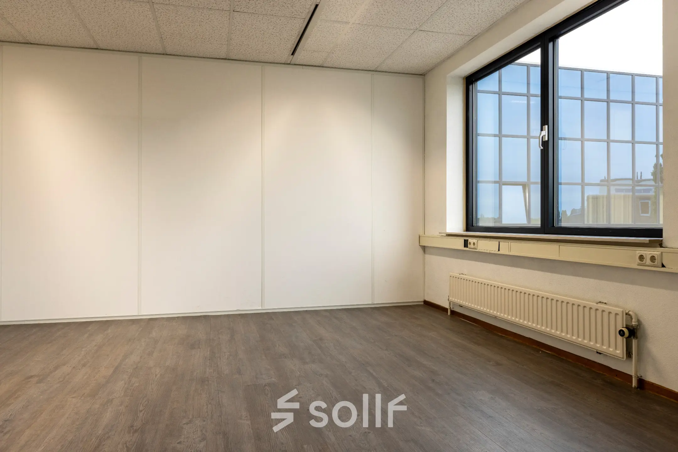 Een lichte kantoorruimte met houten vloer en groot raam aan de Curieweg 9 in Spijkenisse, ideaal voor kantoorruimte huren.