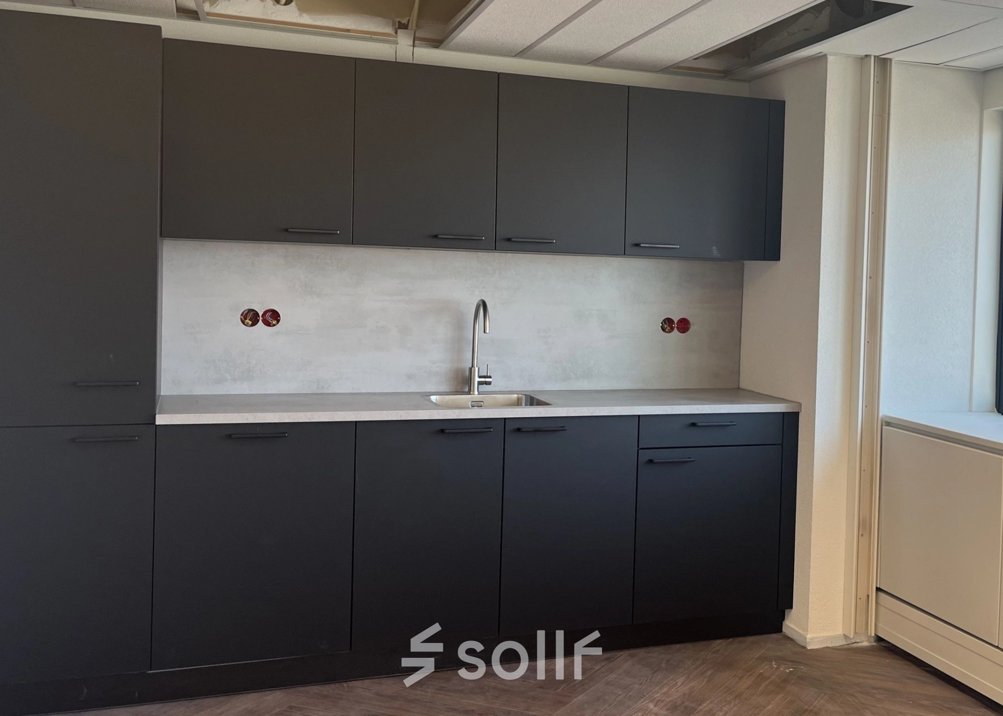 Kantoorruimte te huur met moderne pantry op Jaarbeursplein 22, Utrecht Centraal Station. Voorzien van donkergrijze kasten en een gootsteen.